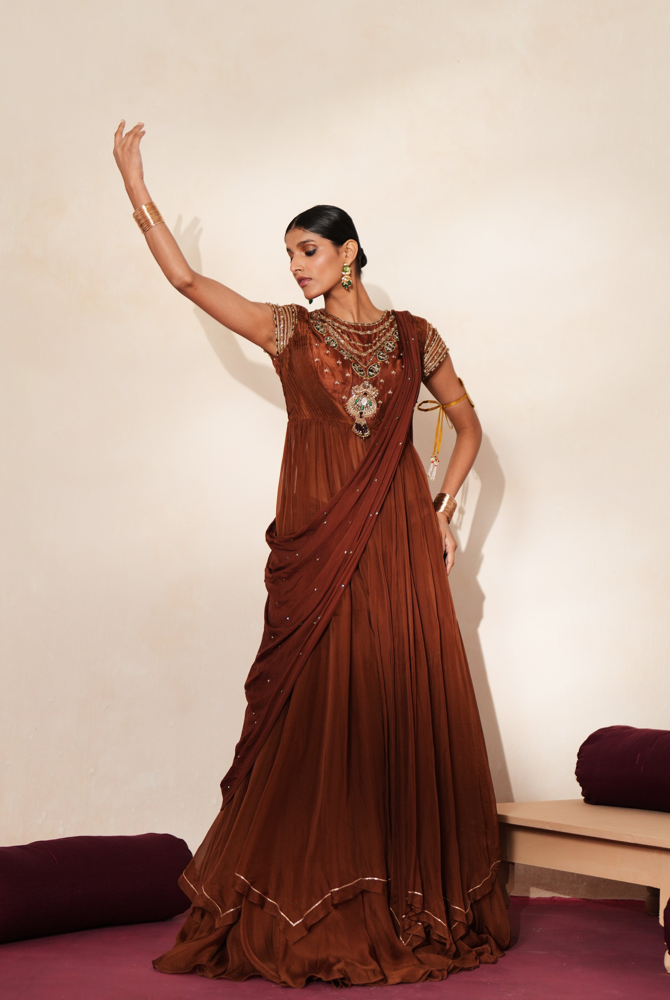 Woman in a mettalic brown traditional outfit standing againsta beige wall on a red carpet.