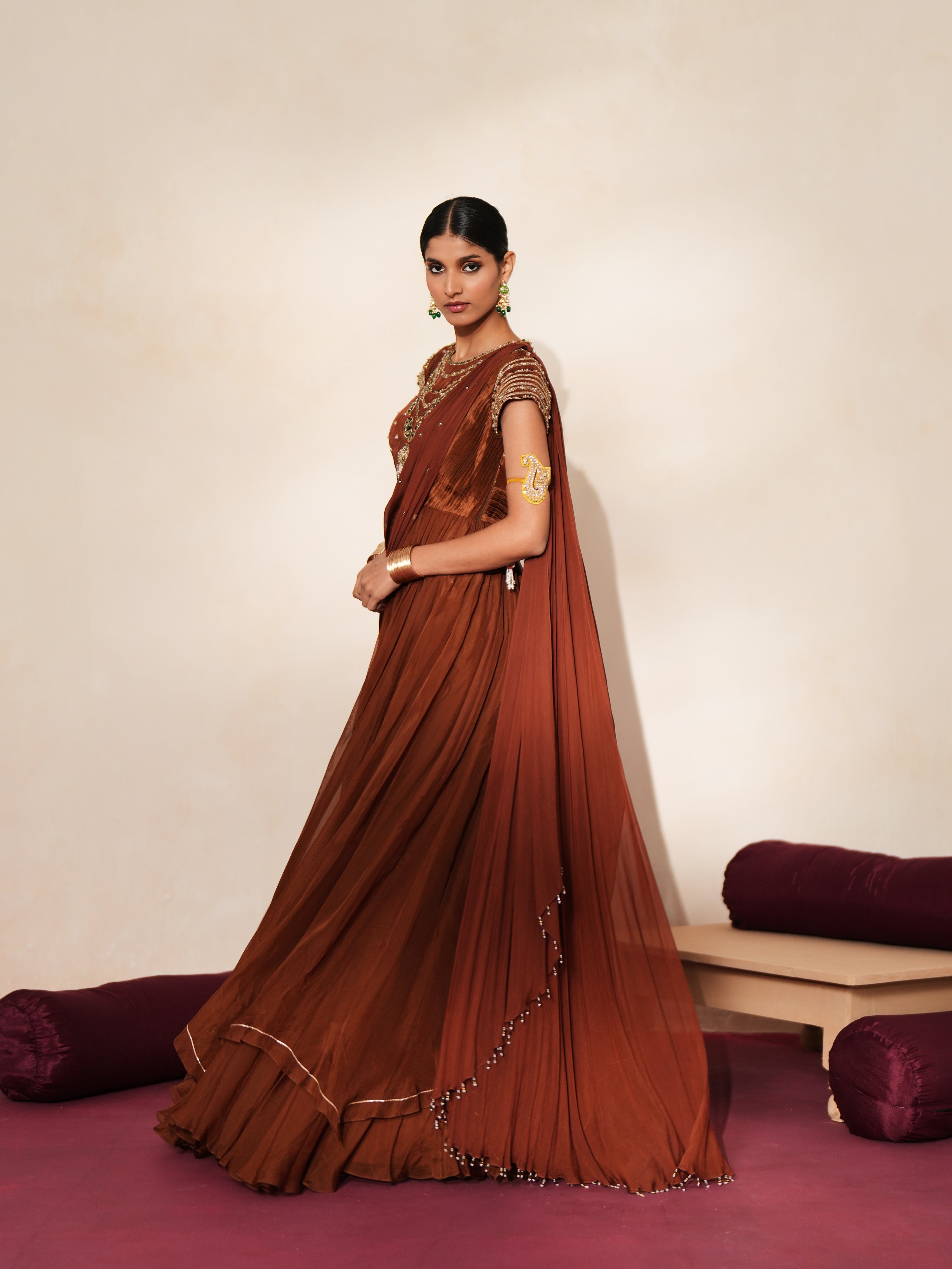 Woman in a mettalic brown traditional outfit standing againsta beige wall on a red carpet.
