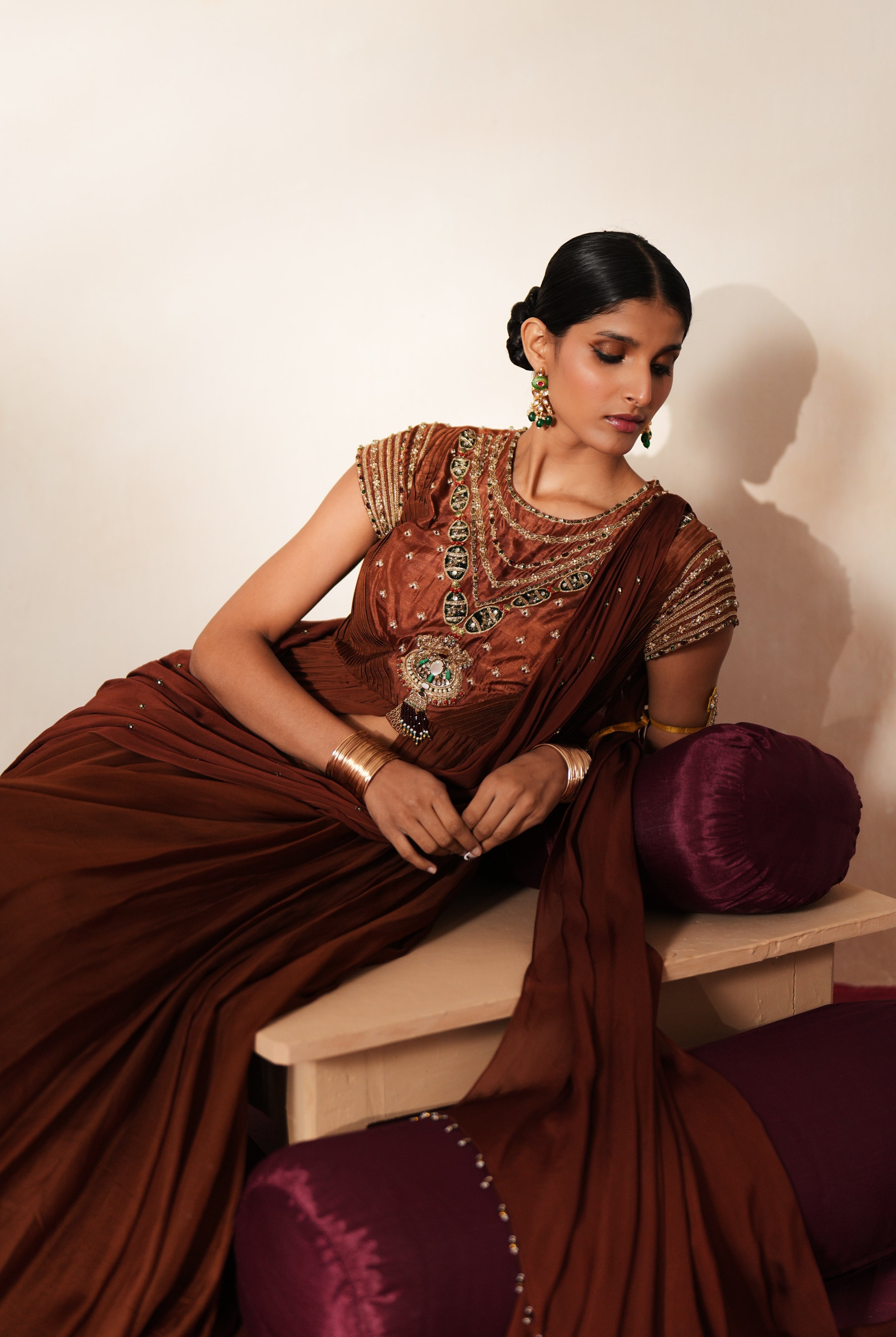 Woman in a mettalic brown traditional outfit standing againsta beige wall on a red carpet.