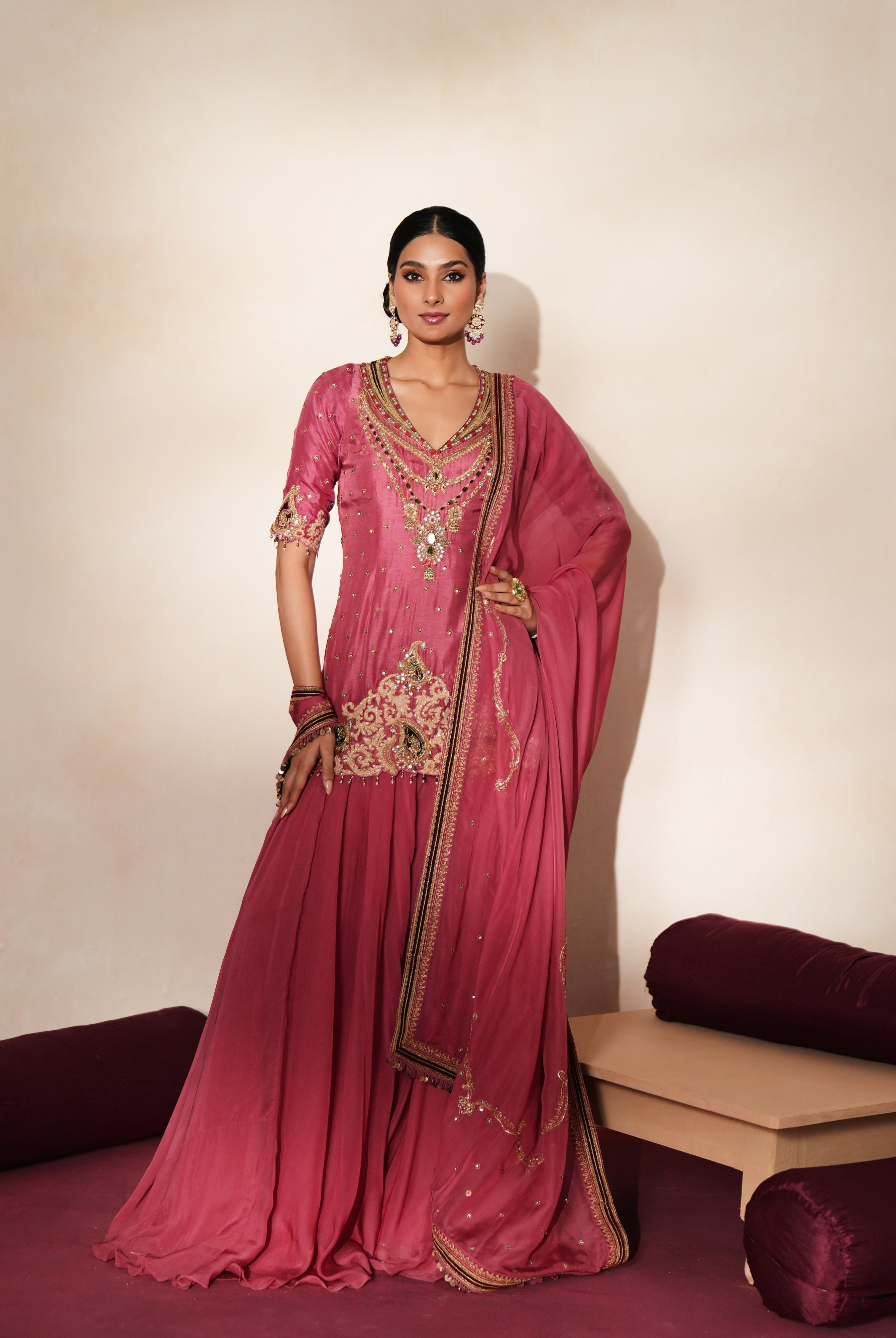 Woman in a mauve pink traditional outfit standing againsta beige wall on a red carpet.