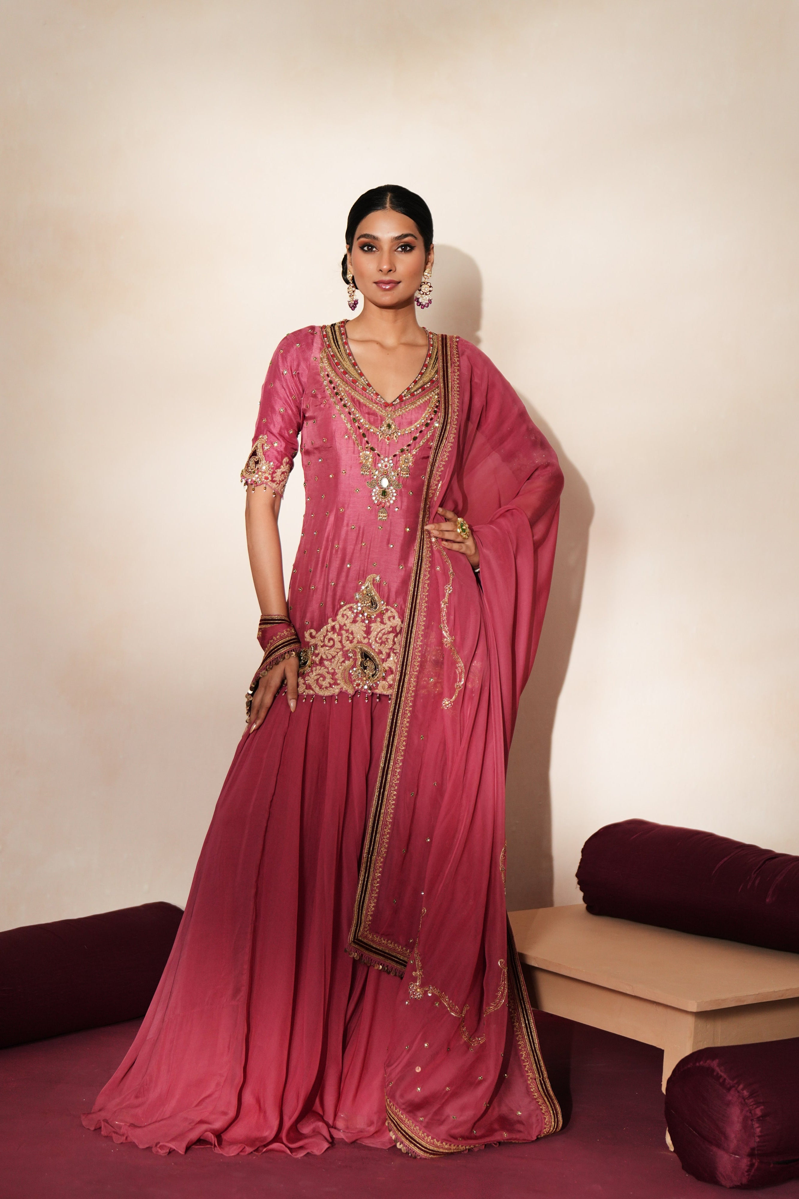 Woman in a mauve pink traditional outfit standing againsta beige wall on a red carpet.