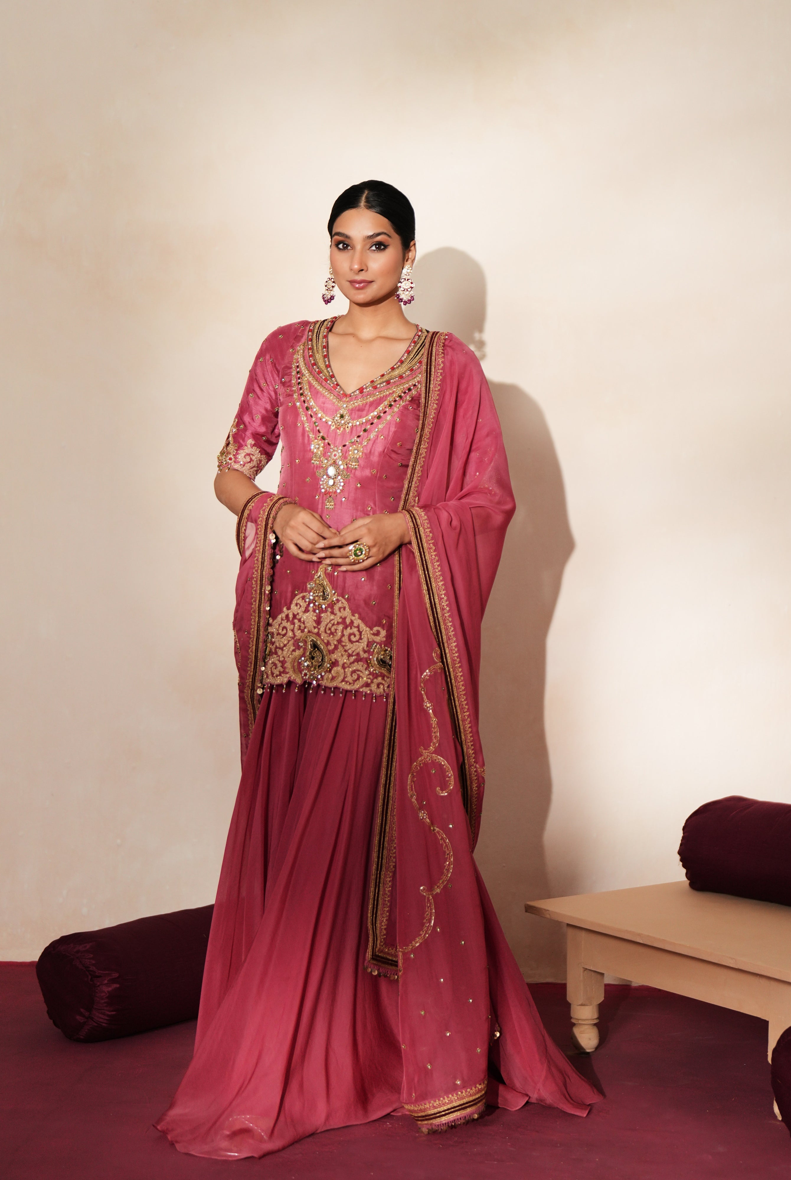 Woman in a mauve pink traditional outfit standing againsta beige wall on a red carpet.