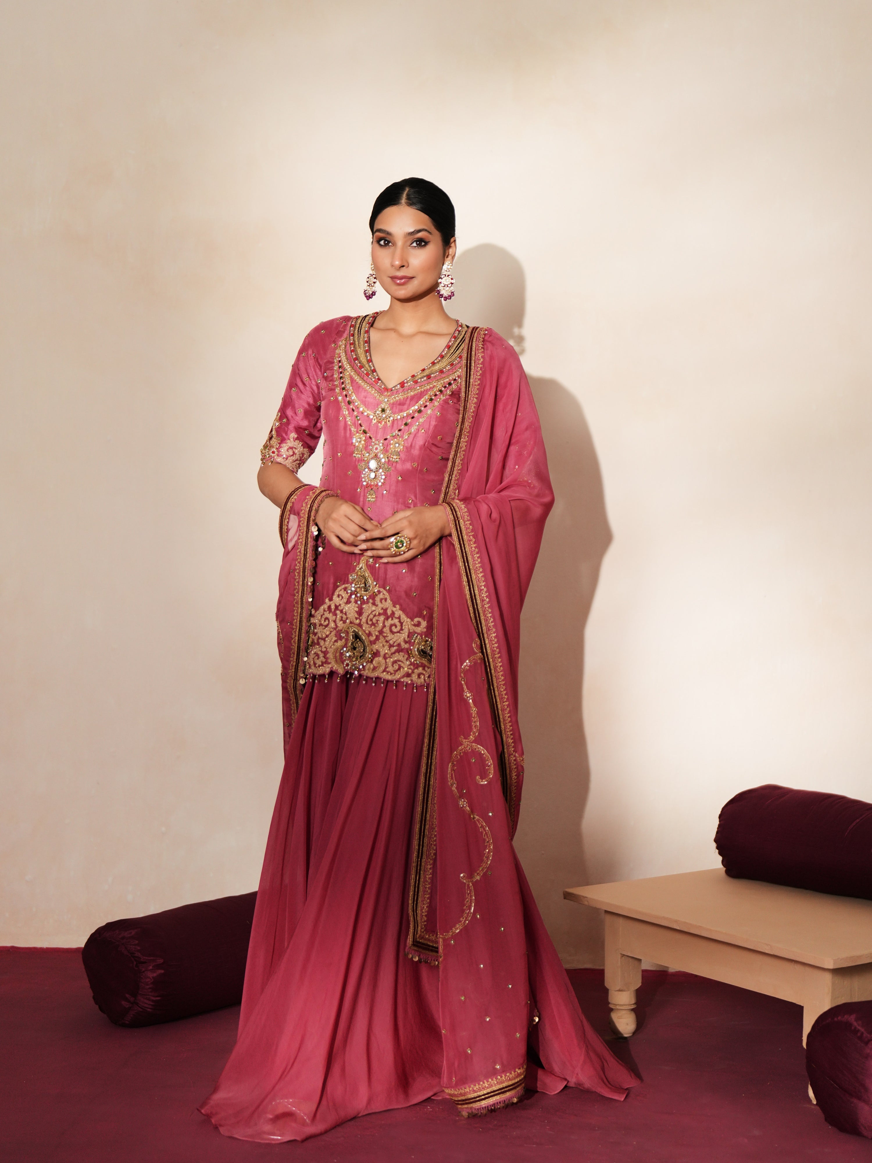 Woman in a mauve pink traditional outfit standing againsta beige wall on a red carpet.