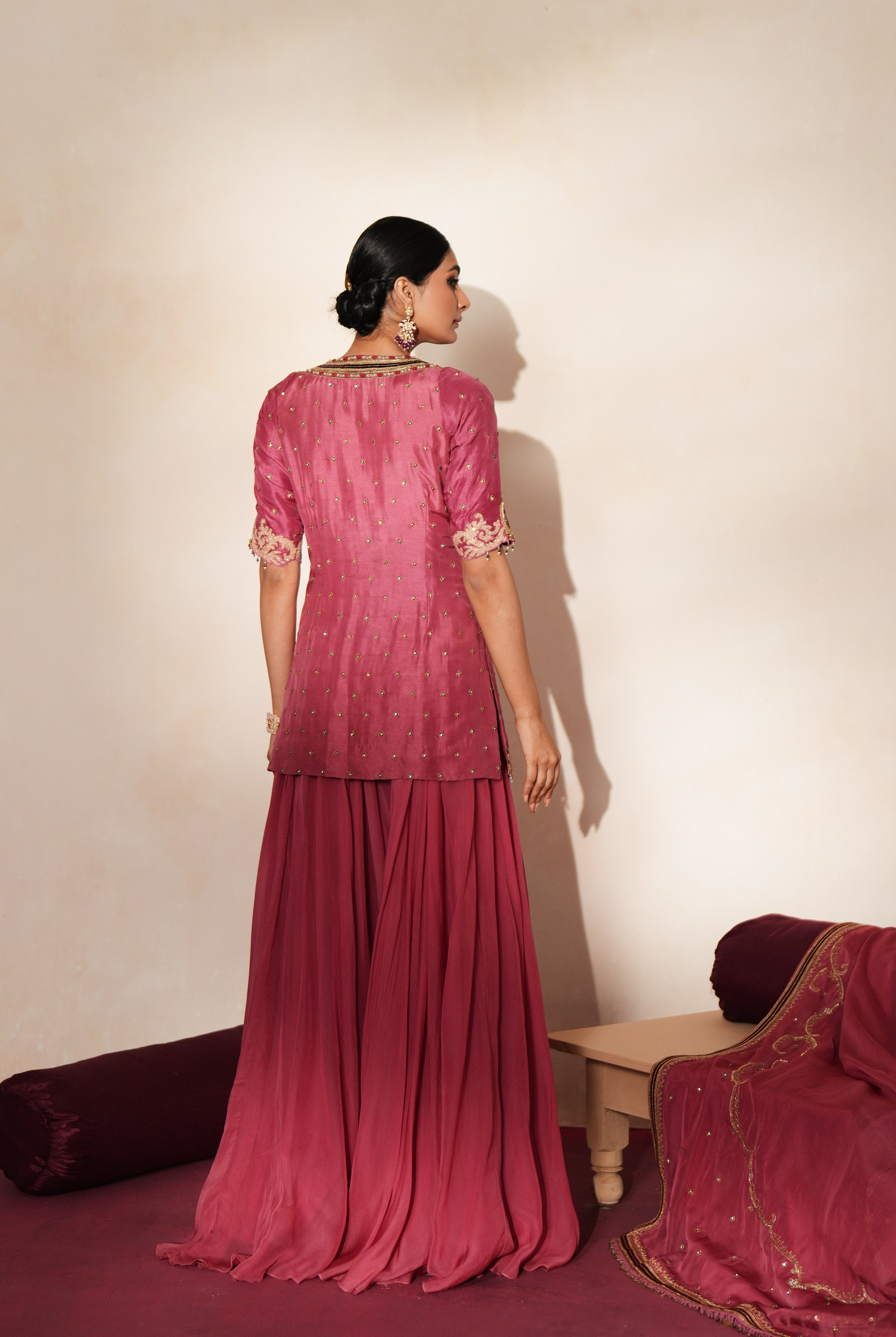 Woman in a mauve pink traditional outfit standing againsta beige wall on a red carpet.