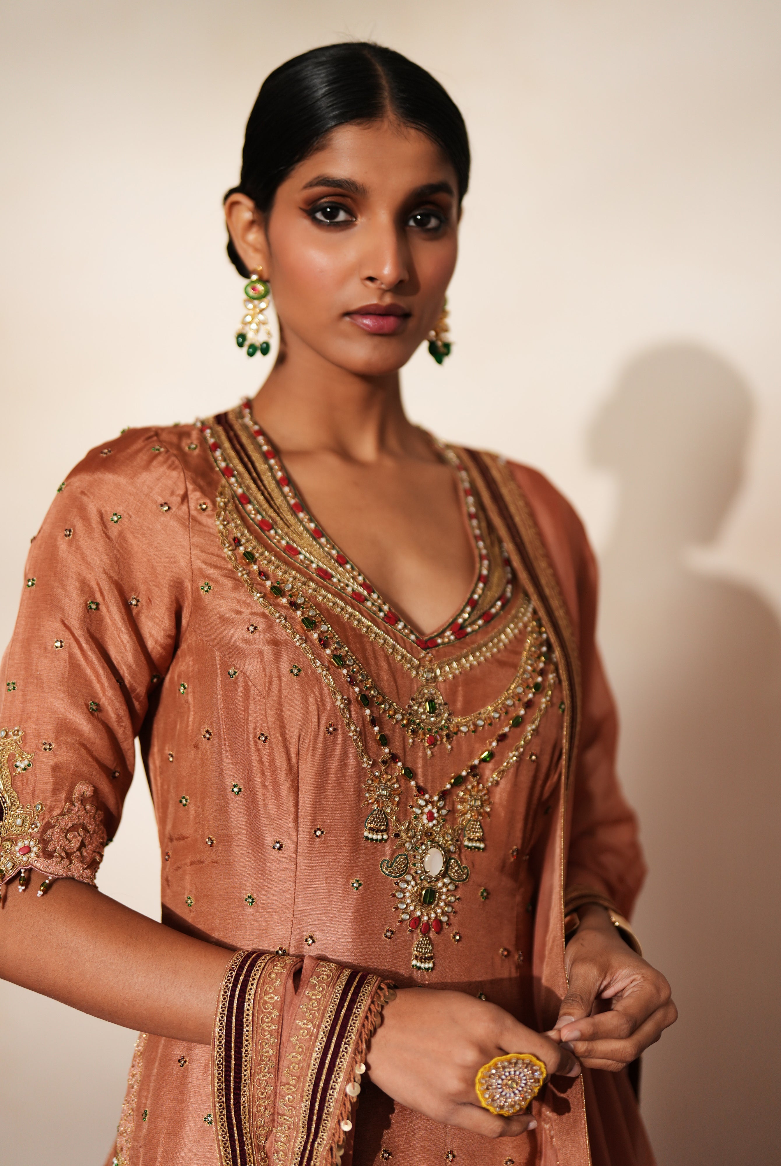 Woman in a metallic mocha traditional outfit standing againsta beige wall on a red carpet.