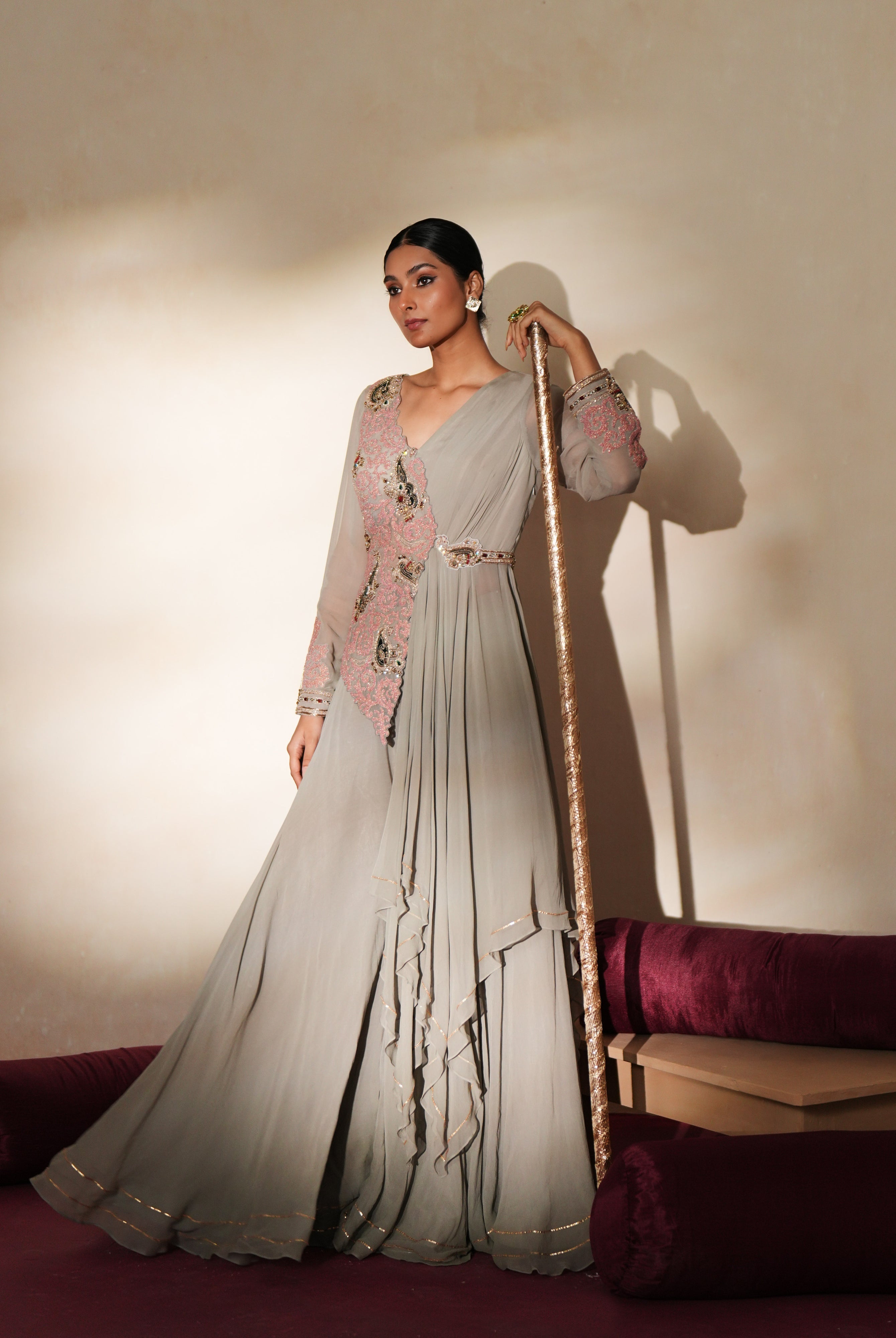 Woman in a mettalic grey traditional outfit standing againsta beige wall on a red carpet.