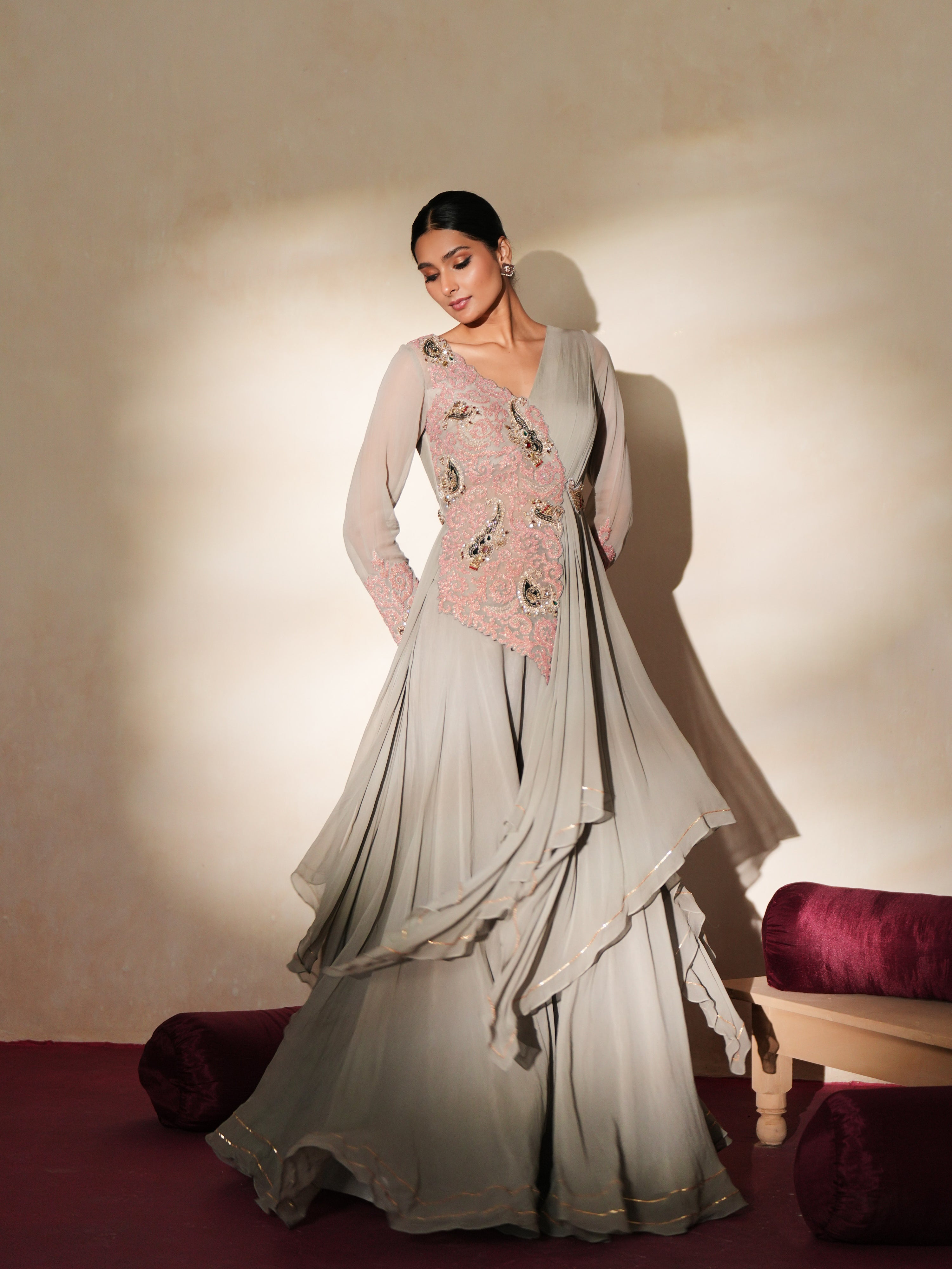 Woman in a mettalic grey traditional outfit standing againsta beige wall on a red carpet.