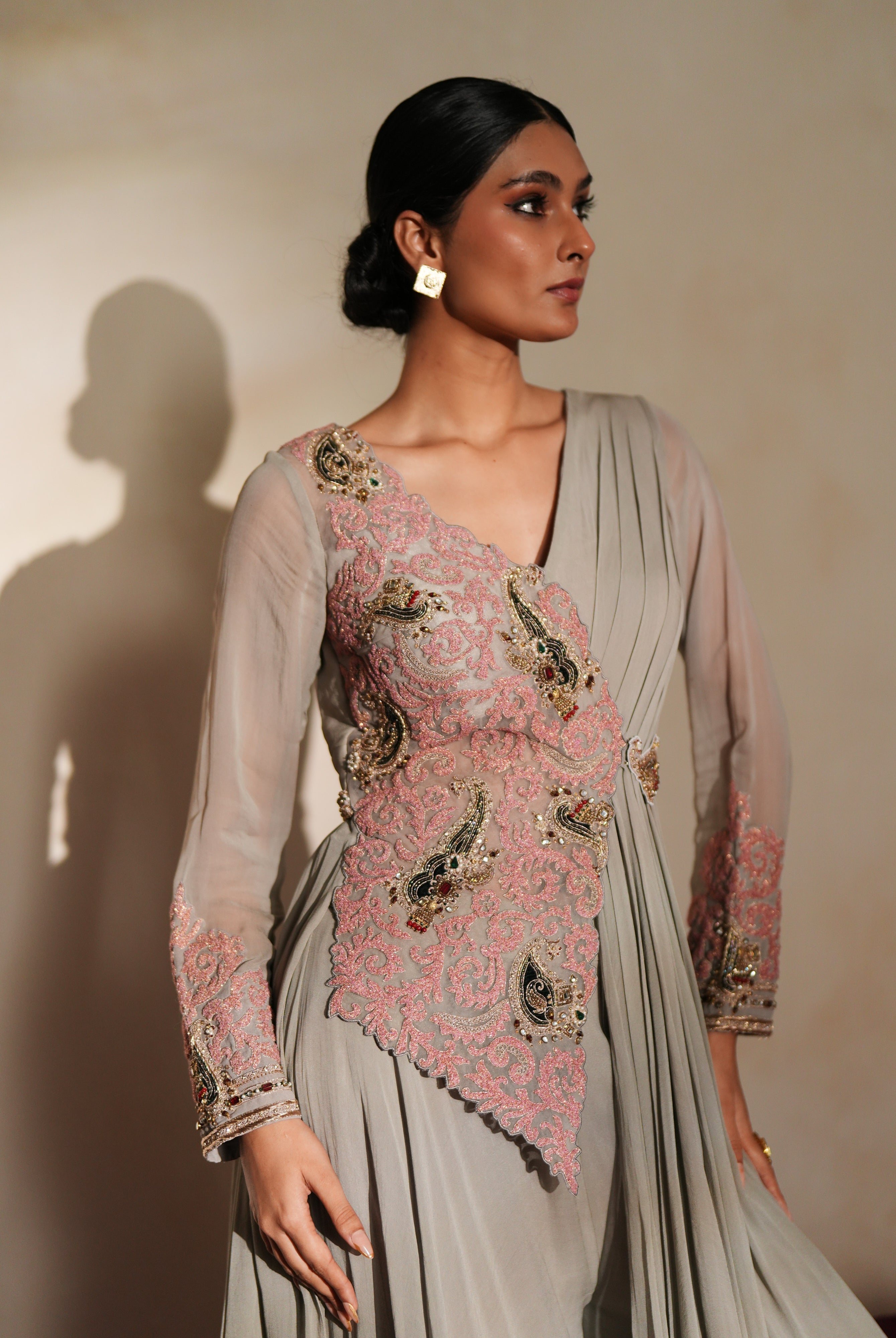 Woman in a mettalic grey traditional outfit standing againsta beige wall on a red carpet.