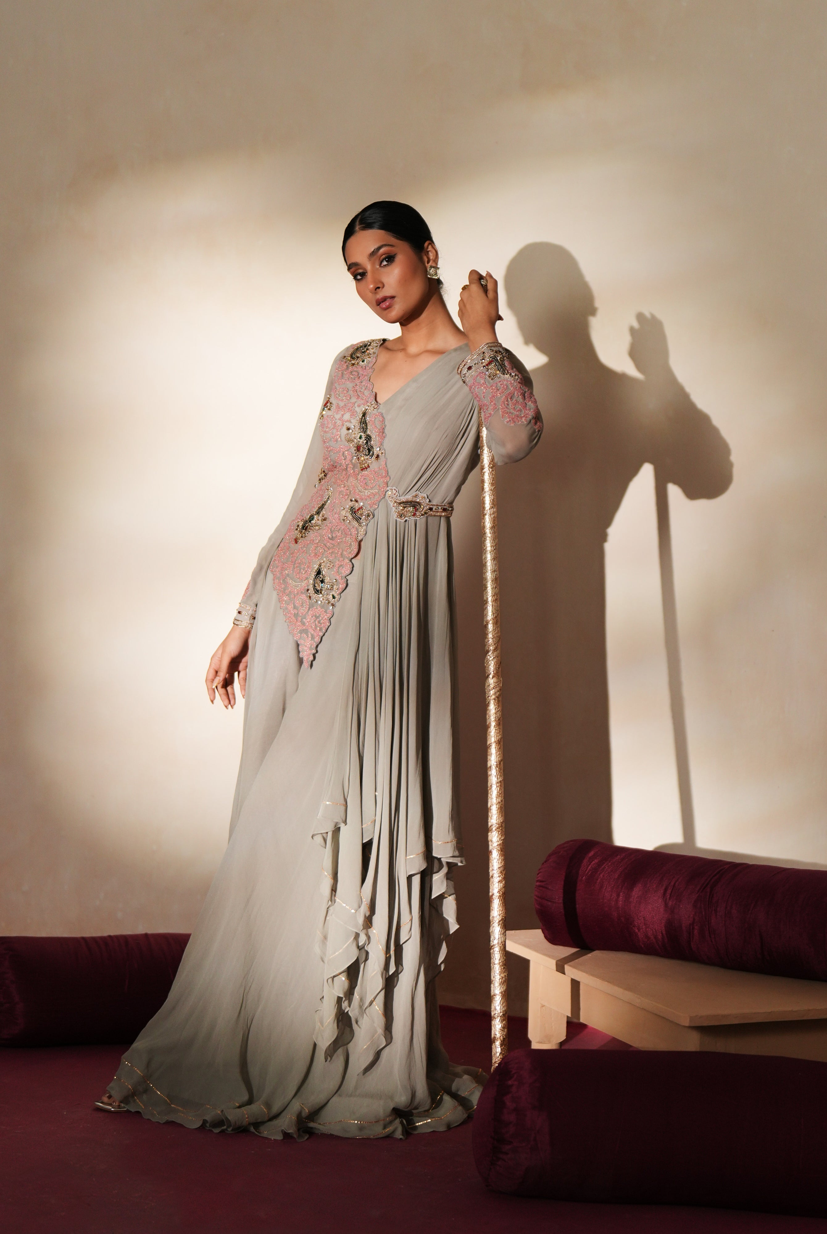Woman in a mettalic grey traditional outfit standing againsta beige wall on a red carpet.