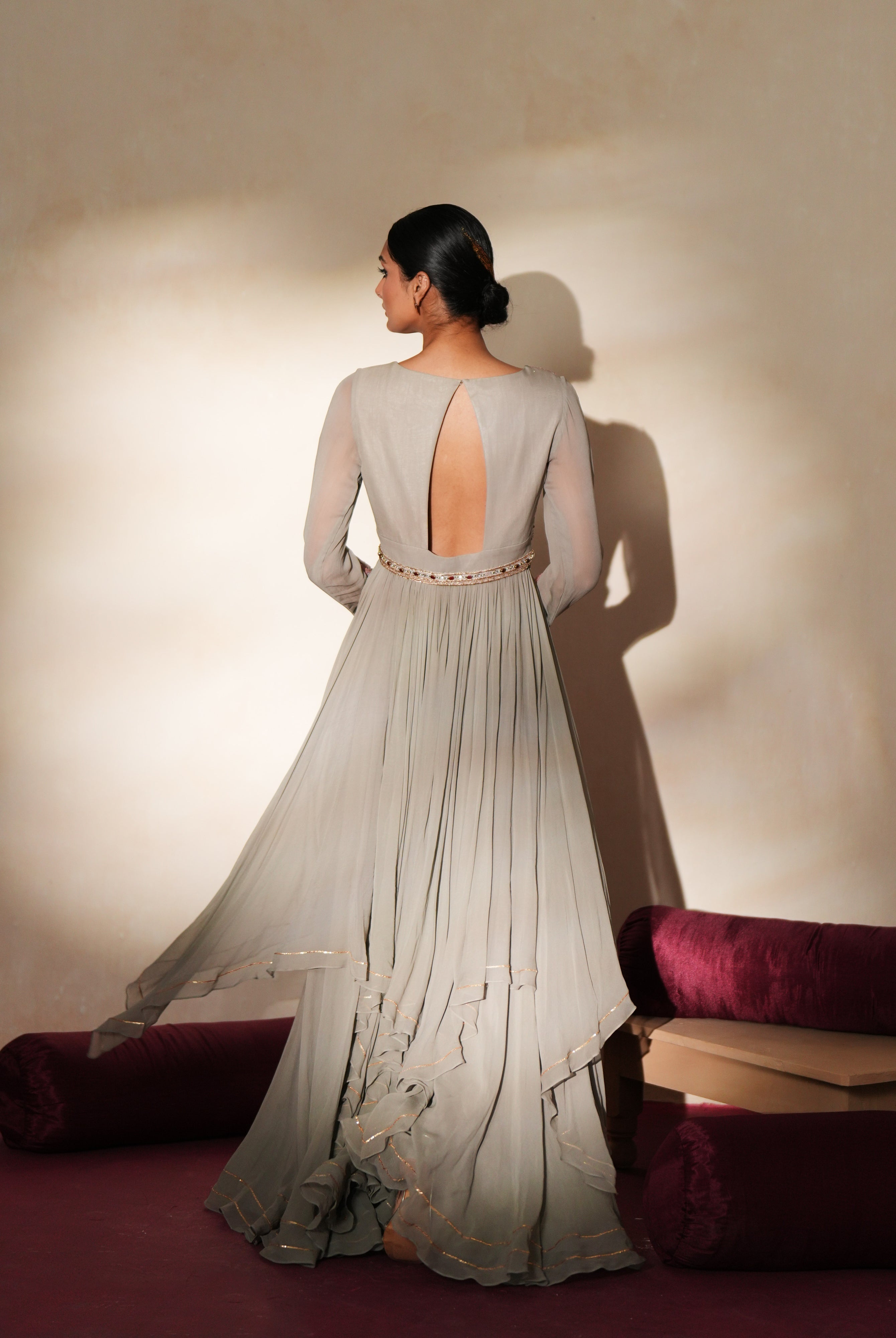 Woman in a mettalic grey traditional outfit standing againsta beige wall on a red carpet.