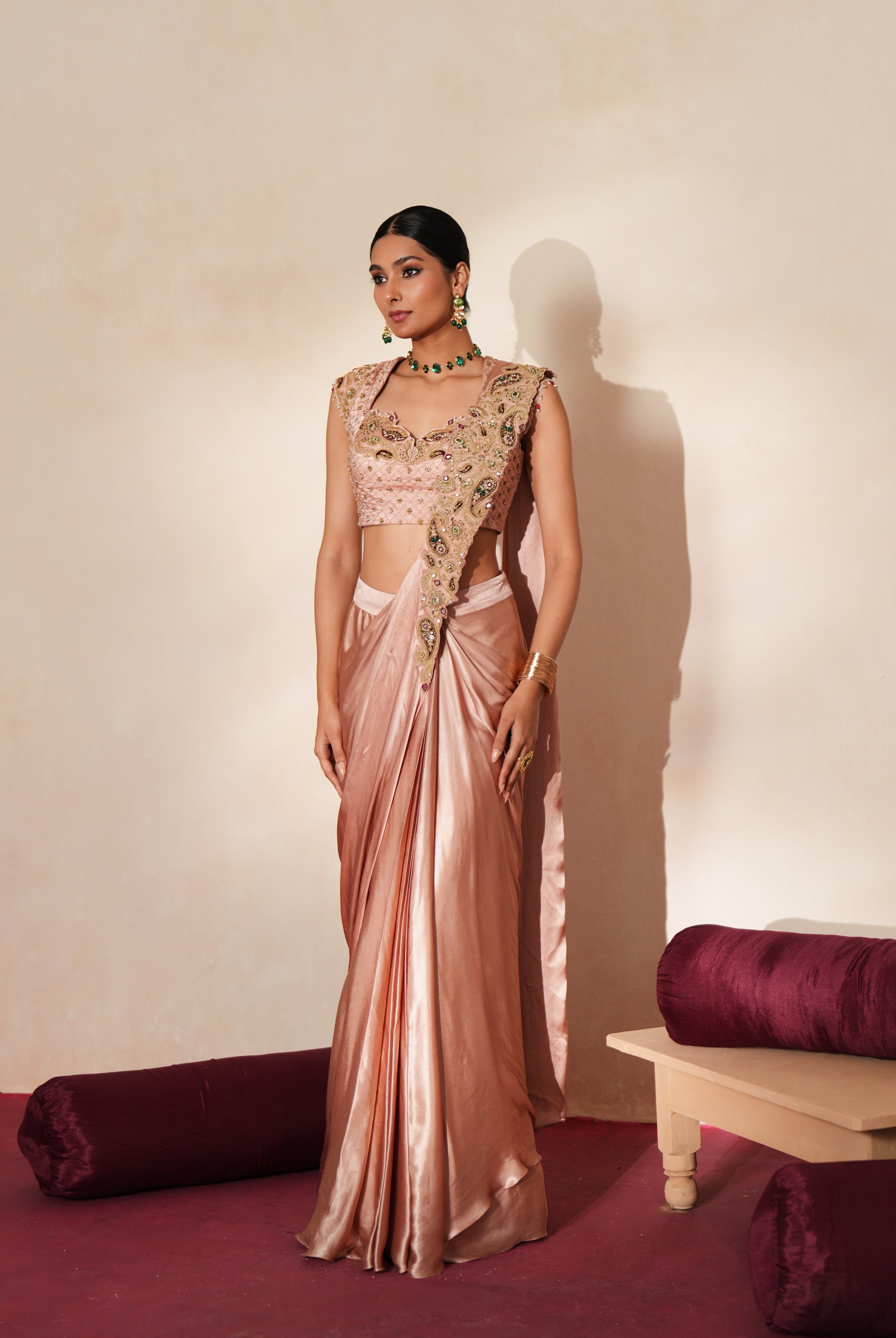 Woman in a soft pink traditional outfit standing againsta beige wall on a red carpet.
