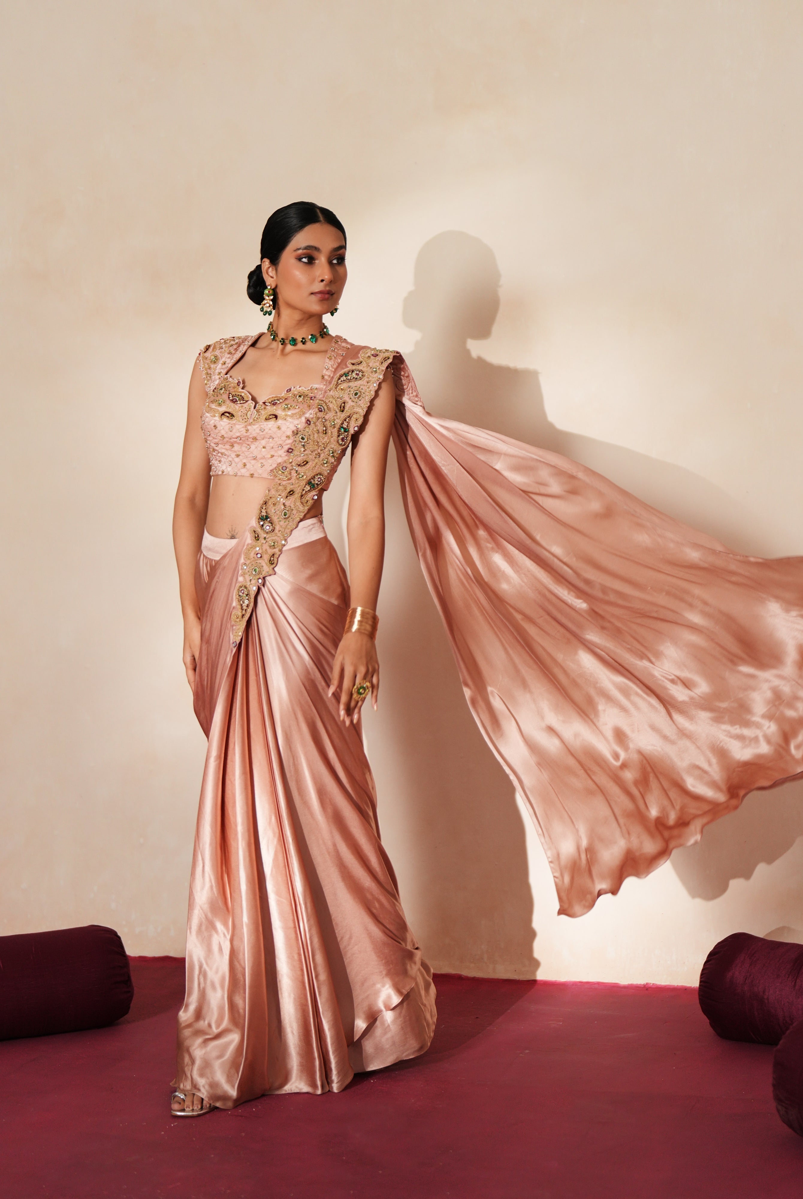 Woman in a soft pink traditional outfit standing againsta beige wall on a red carpet.