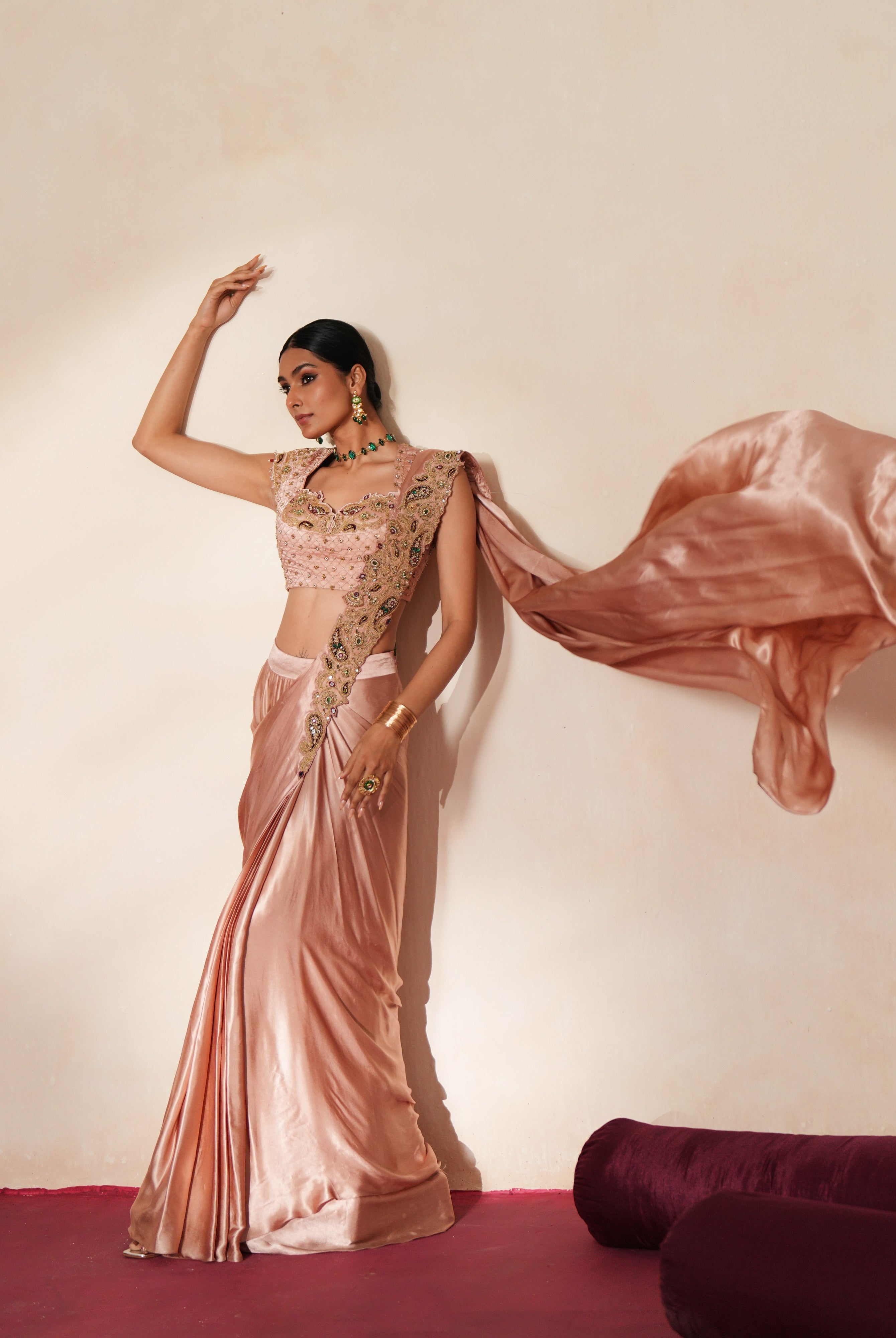 Woman in a soft pink traditional outfit standing againsta beige wall on a red carpet.
