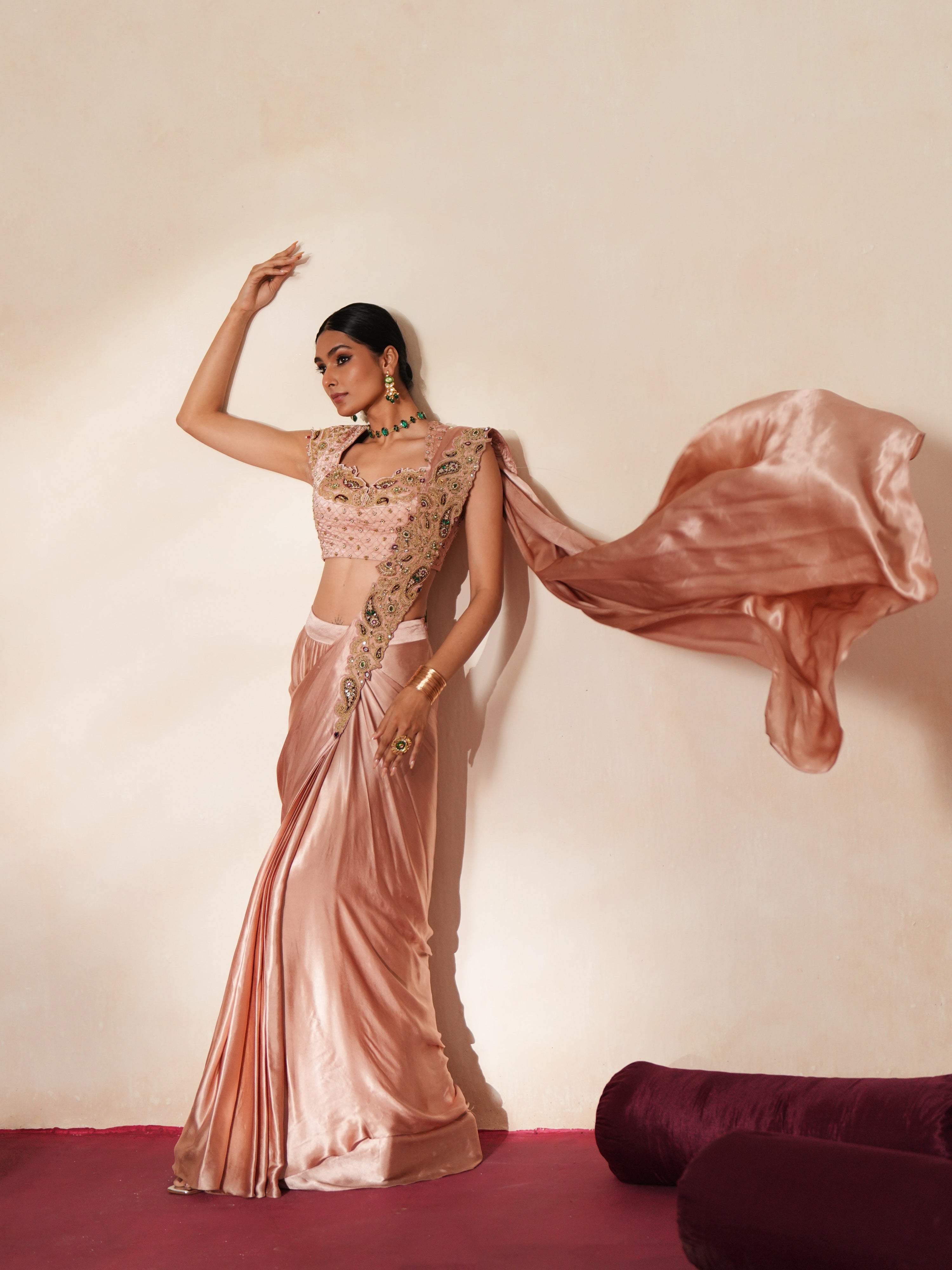 Woman in a soft pink traditional outfit standing againsta beige wall on a red carpet.