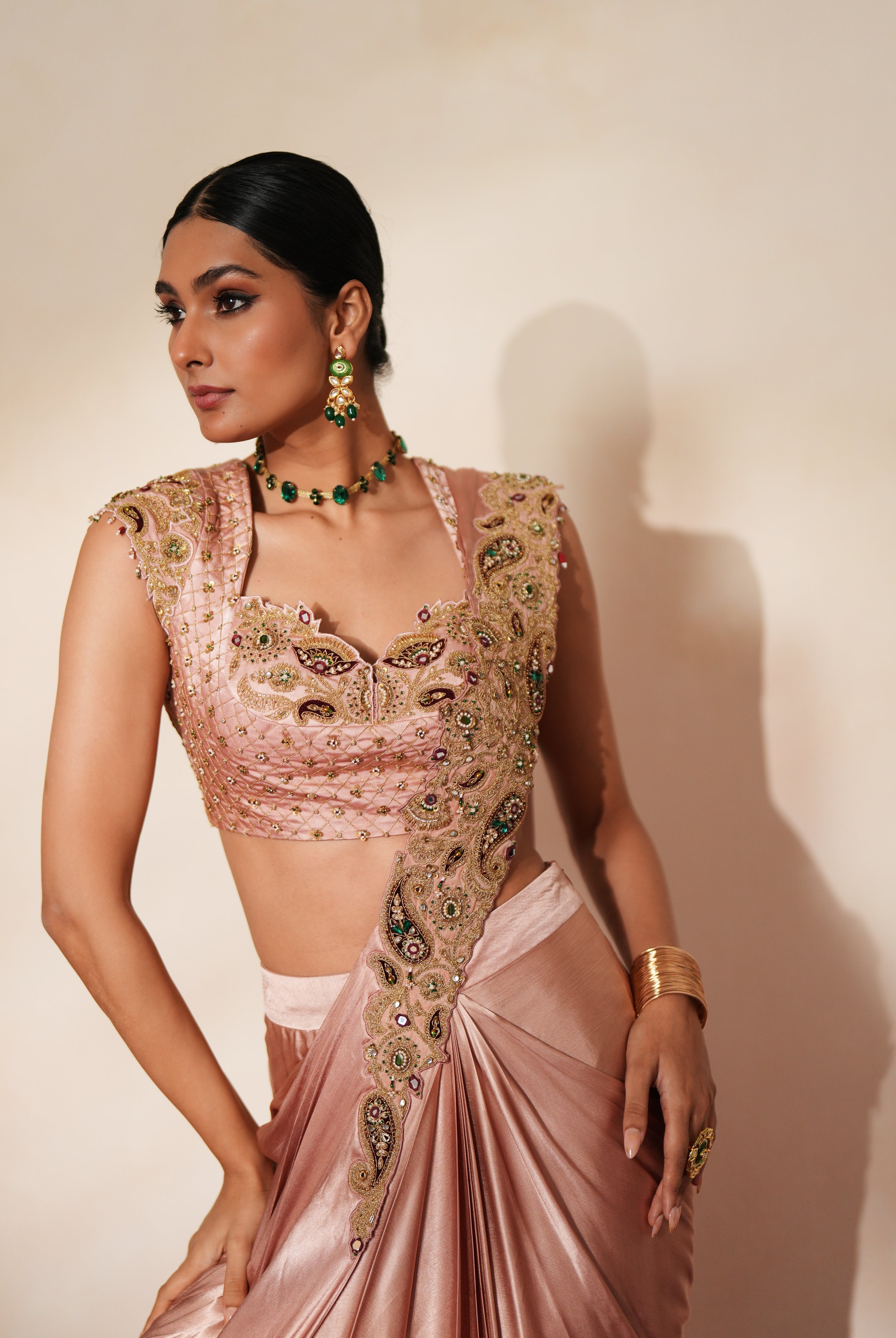 Woman in a soft pink traditional outfit standing againsta beige wall on a red carpet.