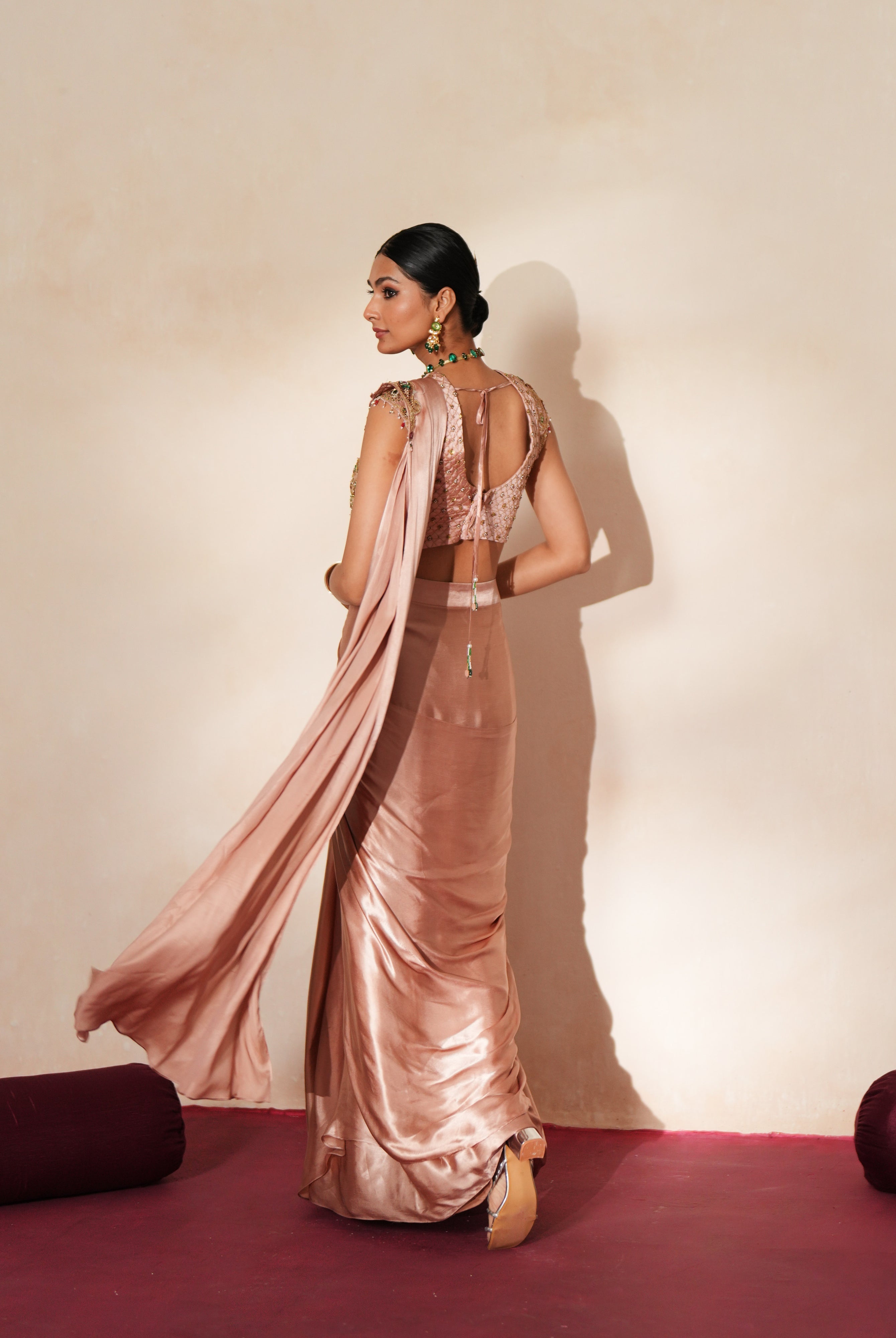 Woman in a soft pink traditional outfit standing againsta beige wall on a red carpet.