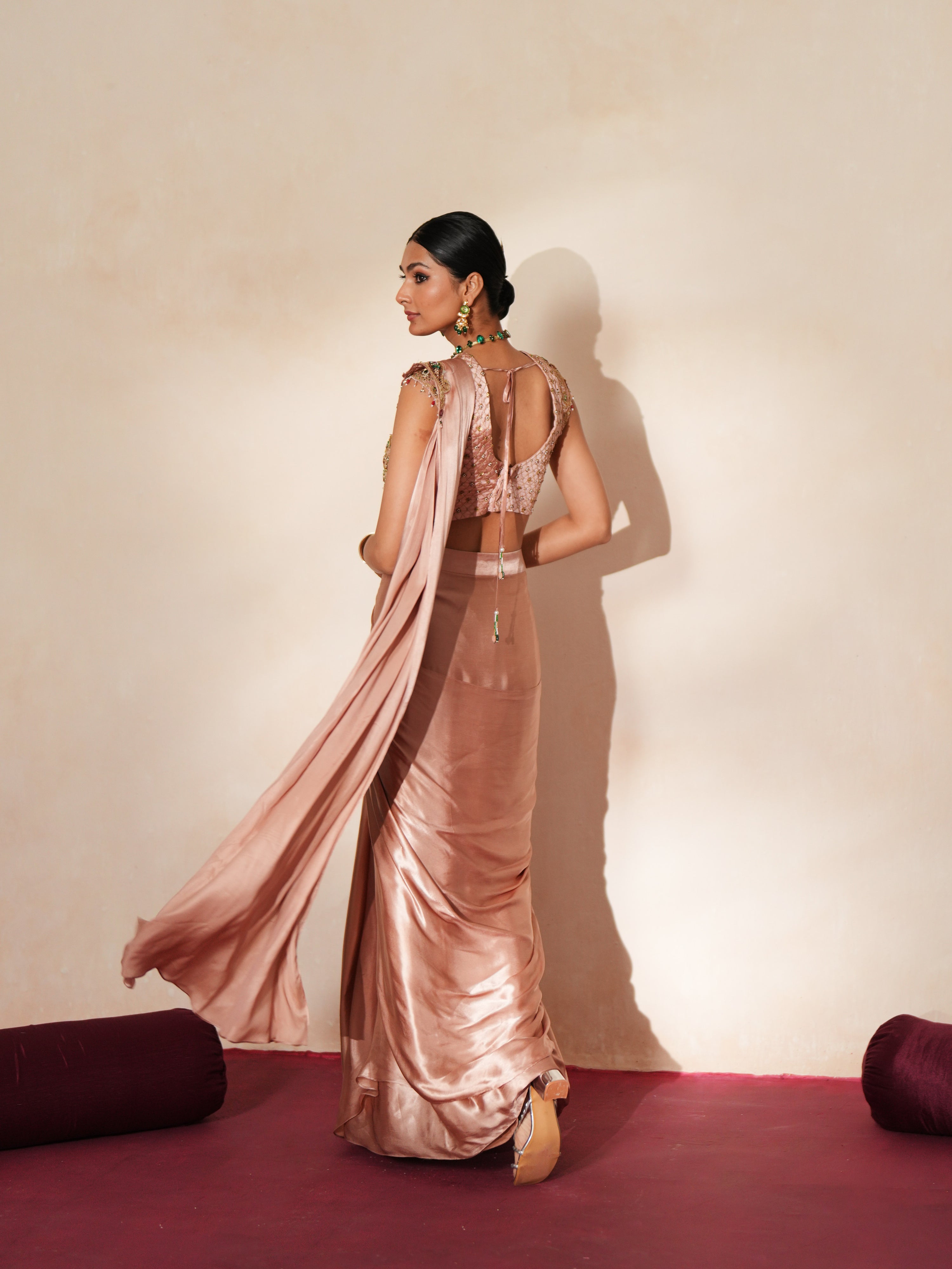Woman in a soft pink traditional outfit standing againsta beige wall on a red carpet.