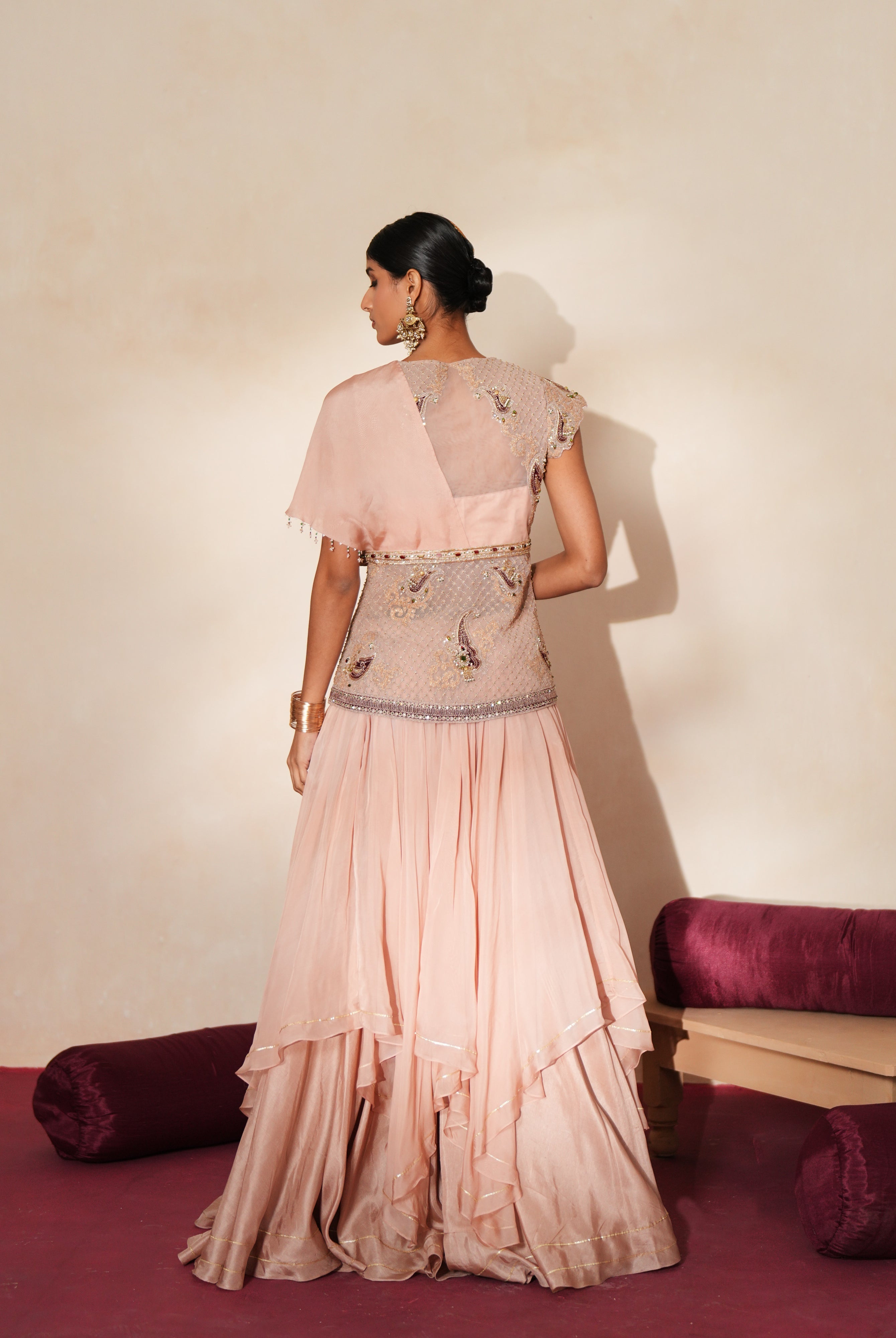 Woman in a soft pink traditional outfit standing againsta beige wall on a red carpet.