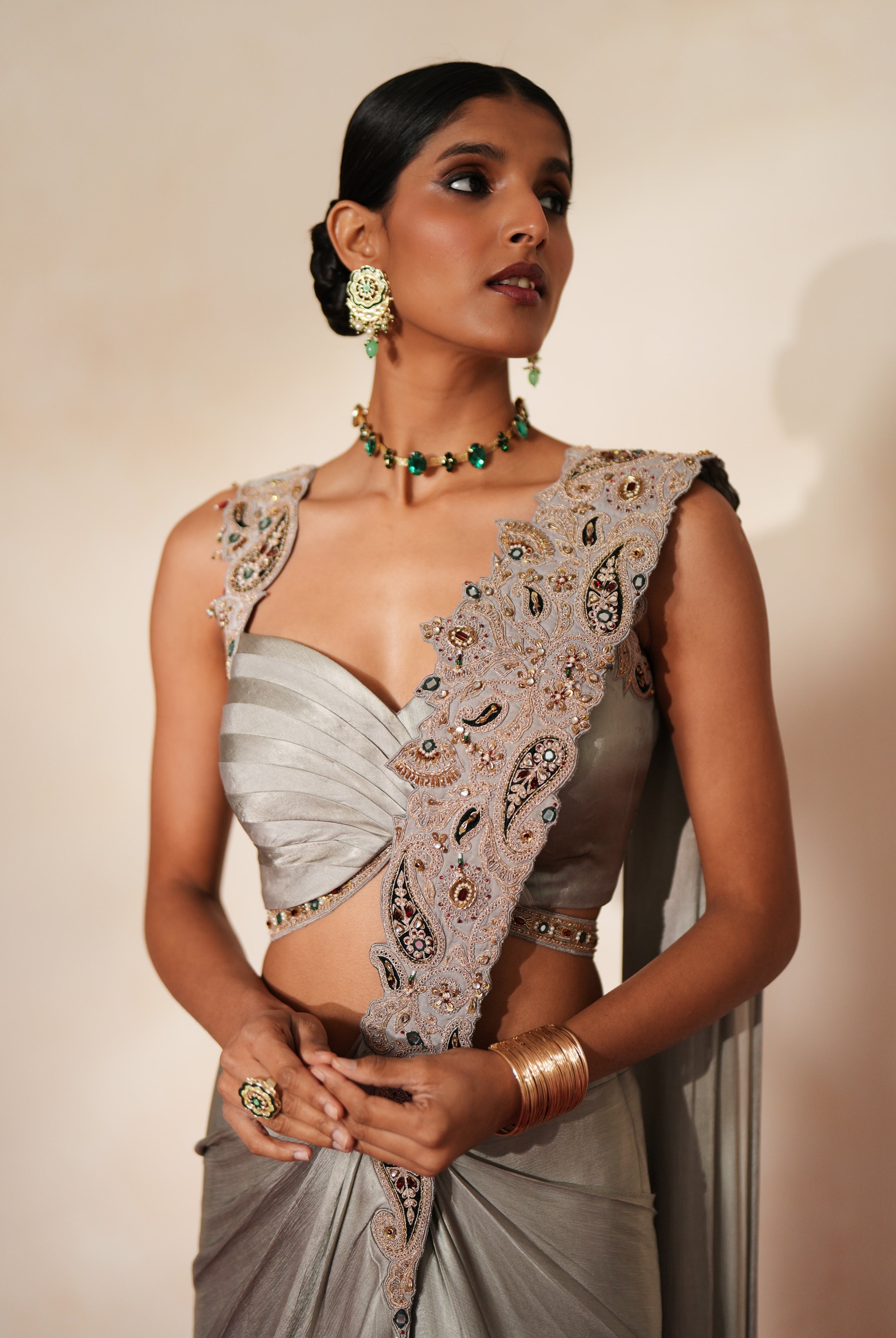Woman in a mettalic grey traditional outfit standing againsta beige wall on a red carpet.