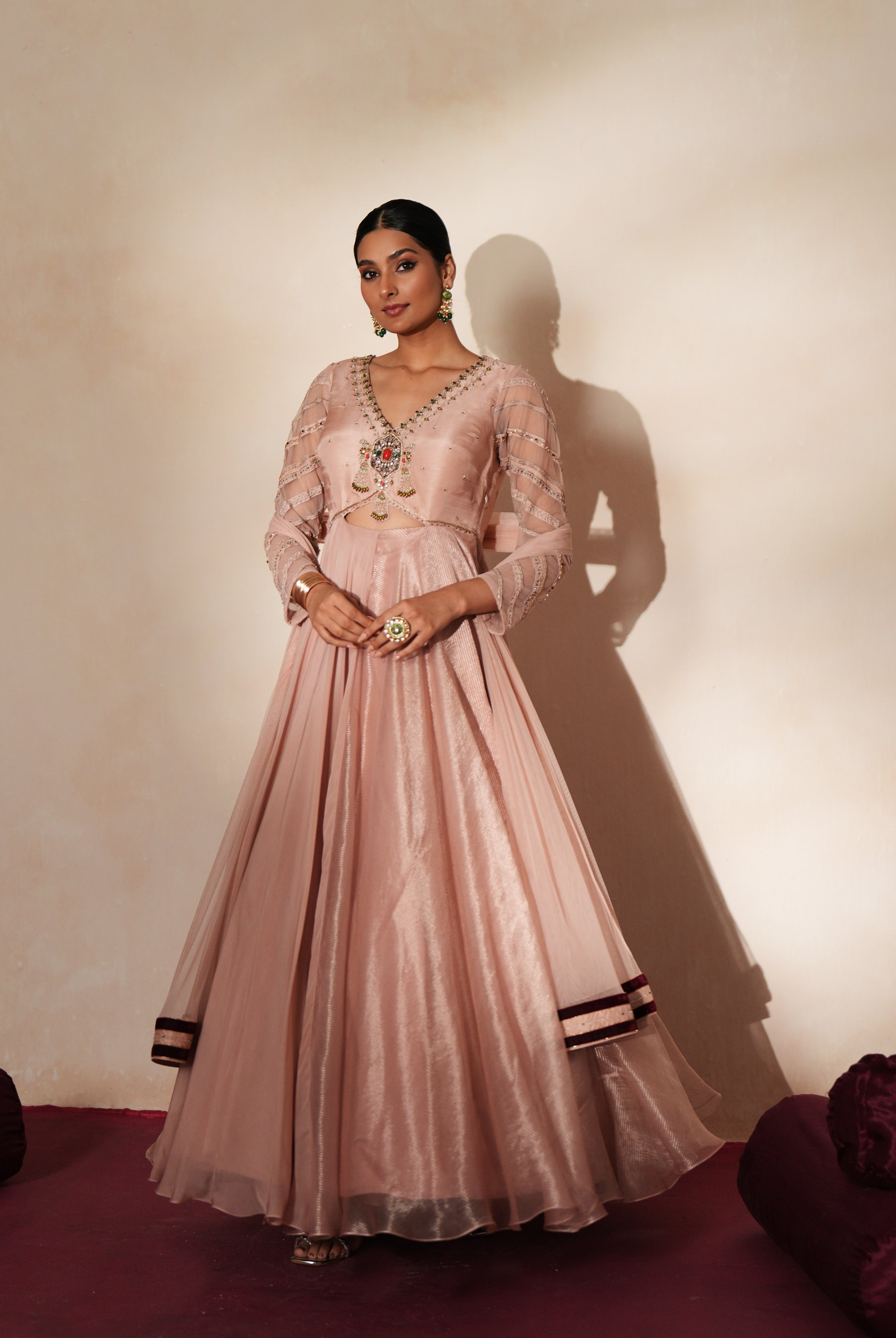 Woman in a soft pink traditional outfit standing againsta beige wall on a red carpet.