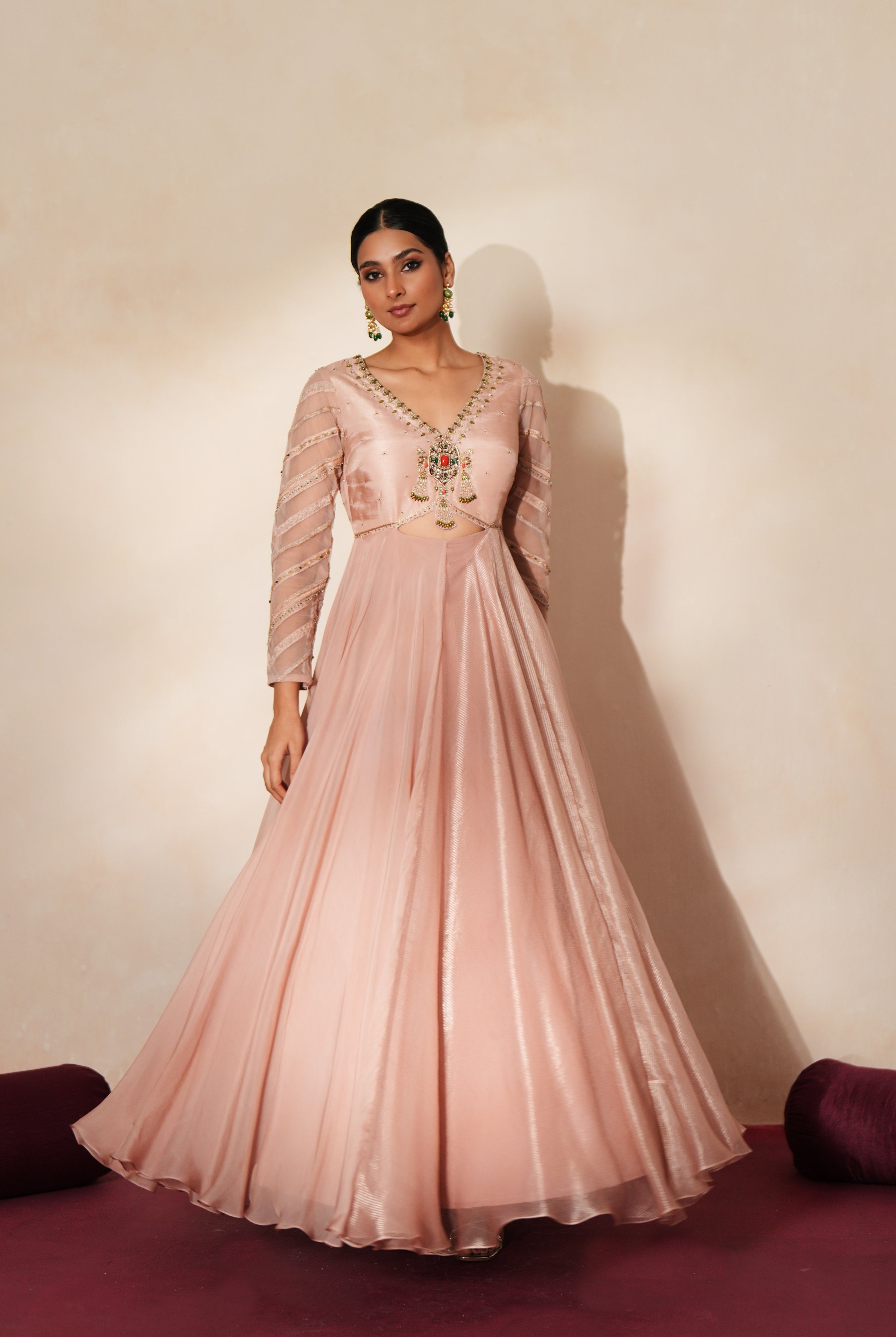 Woman in a soft pink traditional outfit standing againsta beige wall on a red carpet.