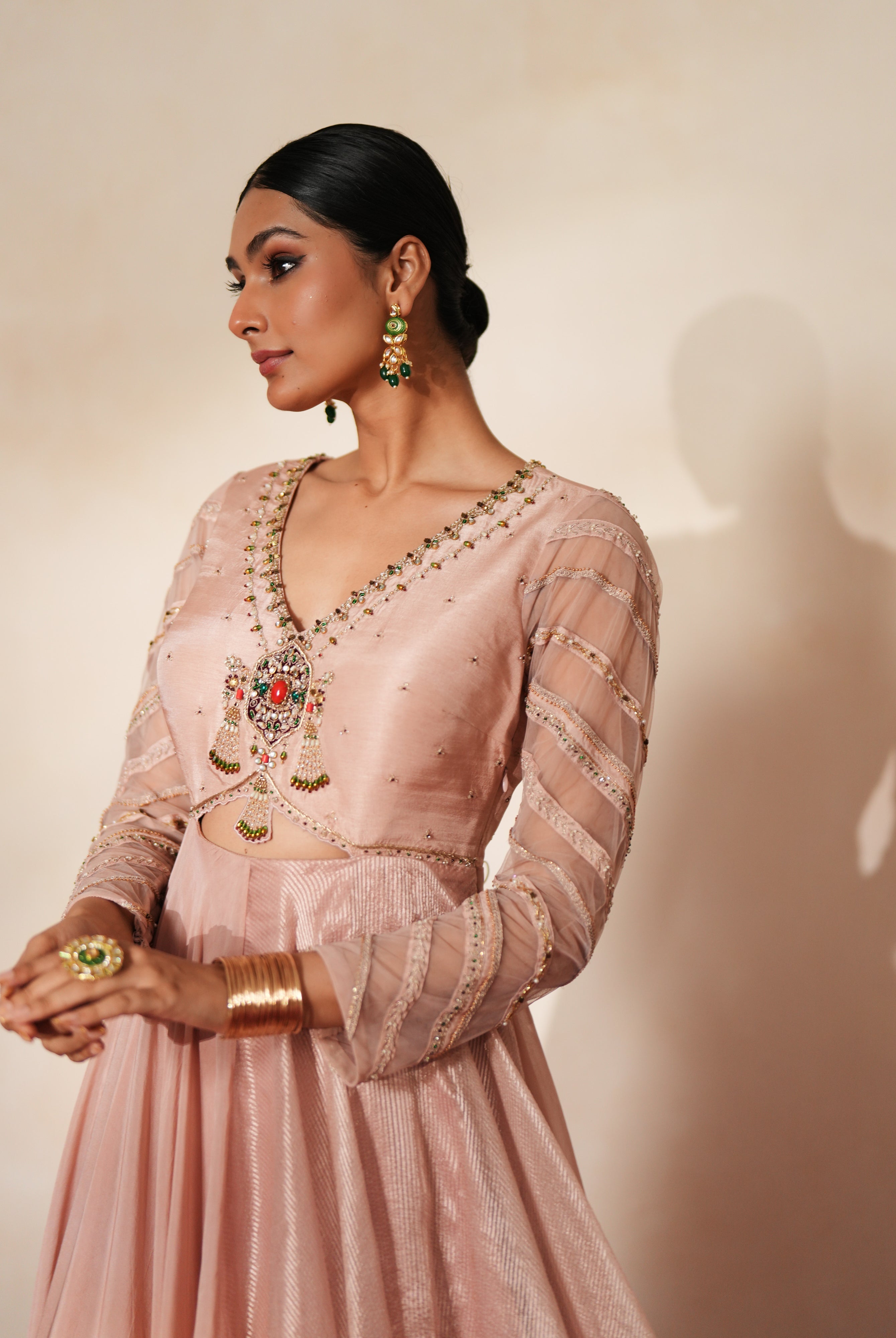 Woman in a soft pink traditional outfit standing againsta beige wall on a red carpet.