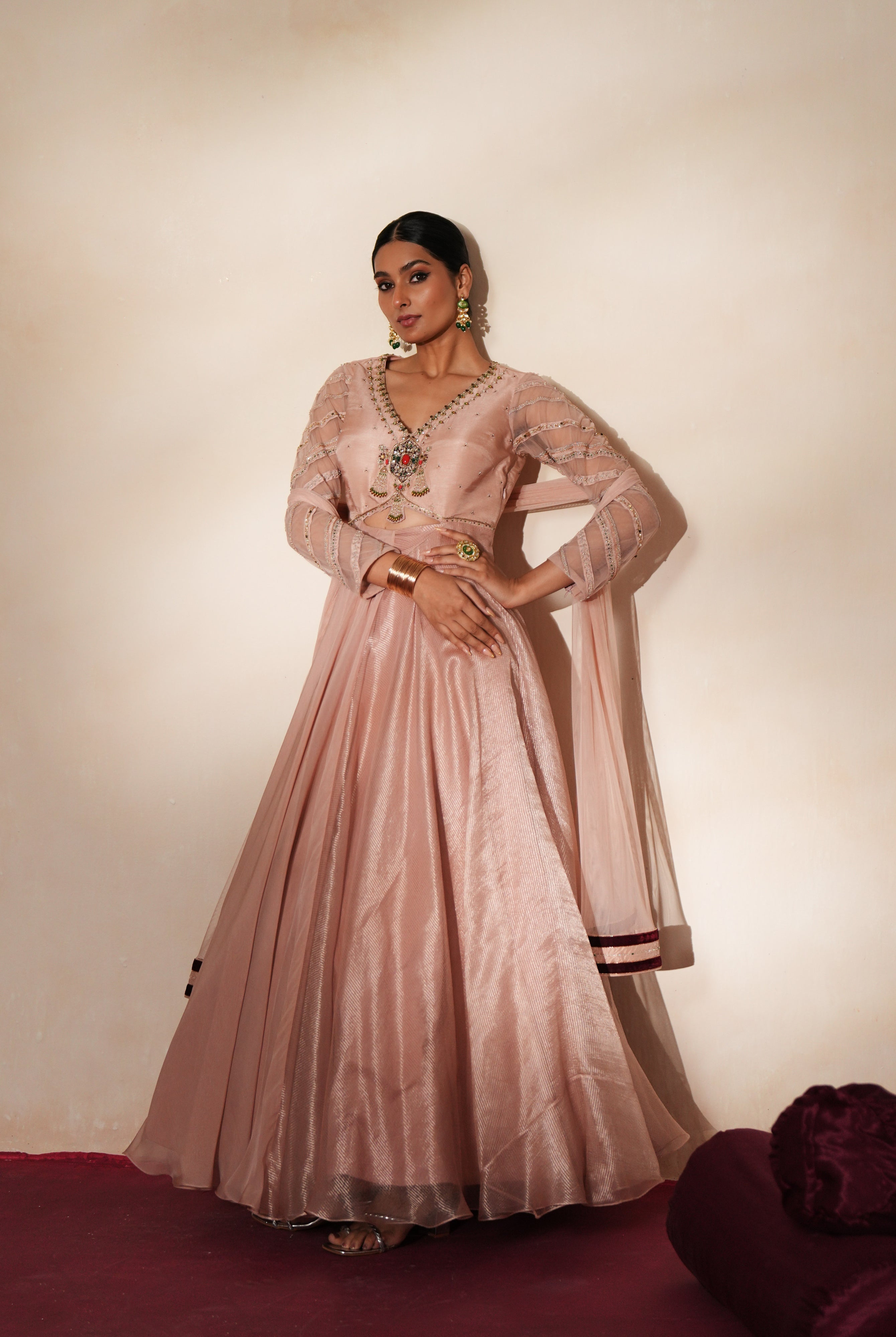 Woman in a soft pink traditional outfit standing againsta beige wall on a red carpet.