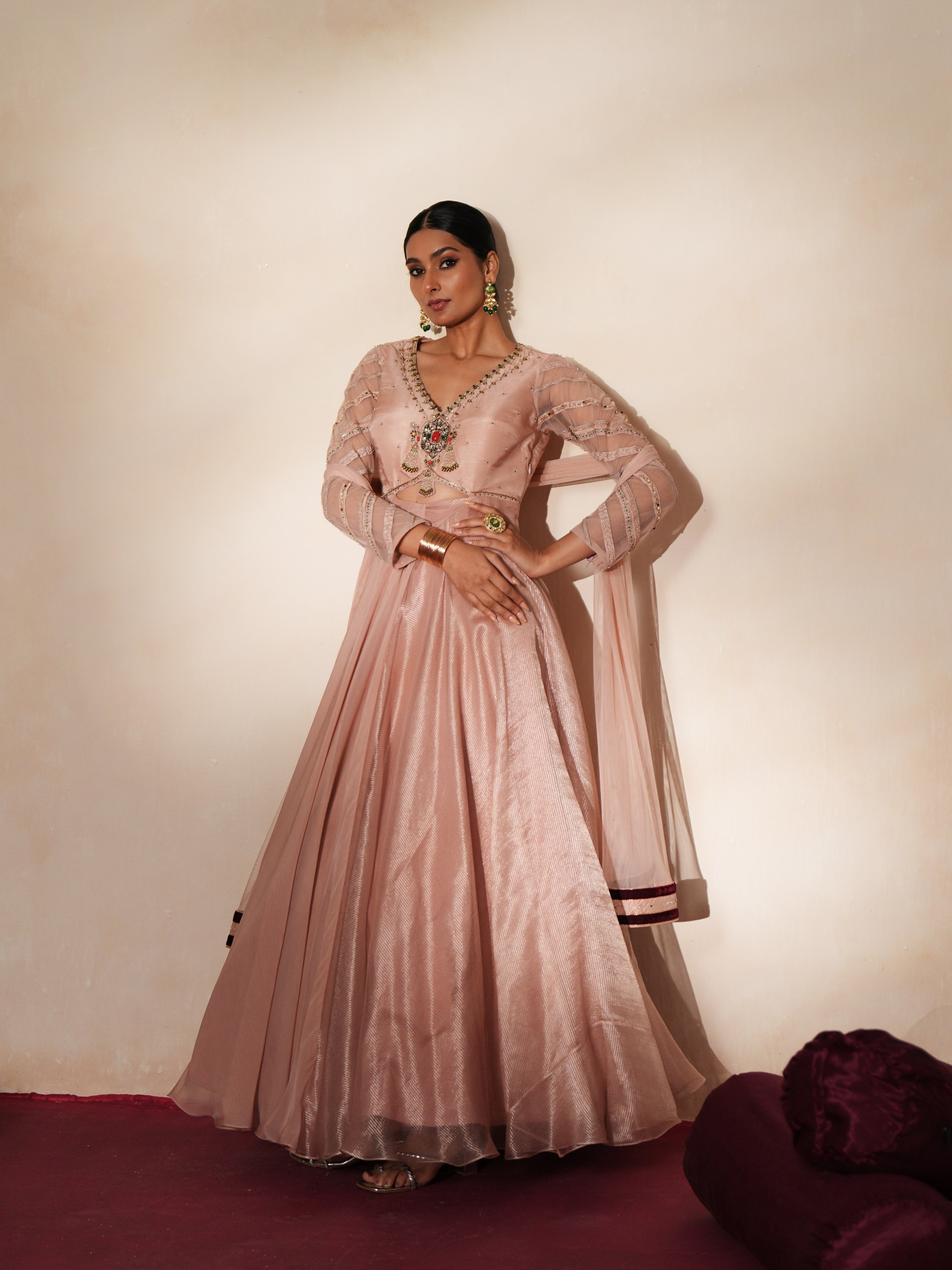 Woman in a soft pink traditional outfit standing againsta beige wall on a red carpet.