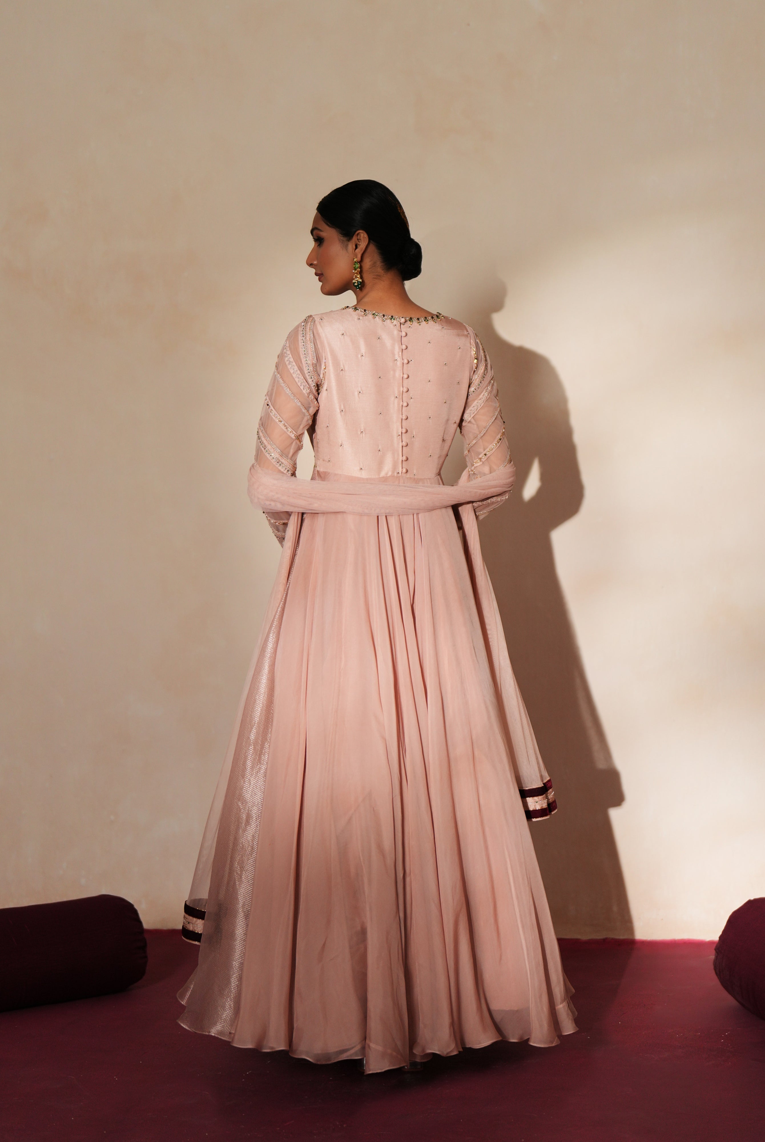 Woman in a soft pink traditional outfit standing againsta beige wall on a red carpet.