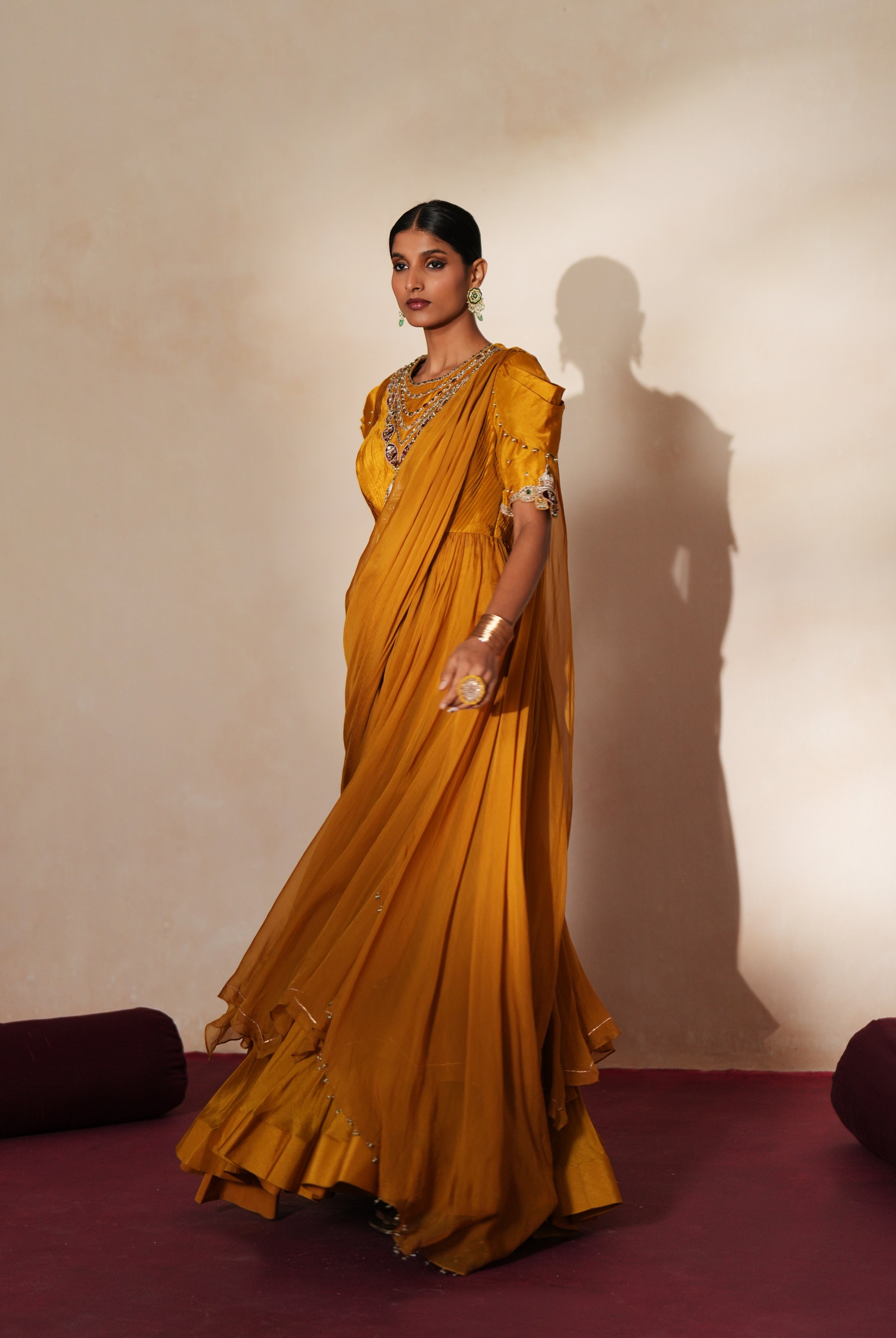 Woman in a golden yellow traditional outfit standing againsta beige wall on a red carpet.