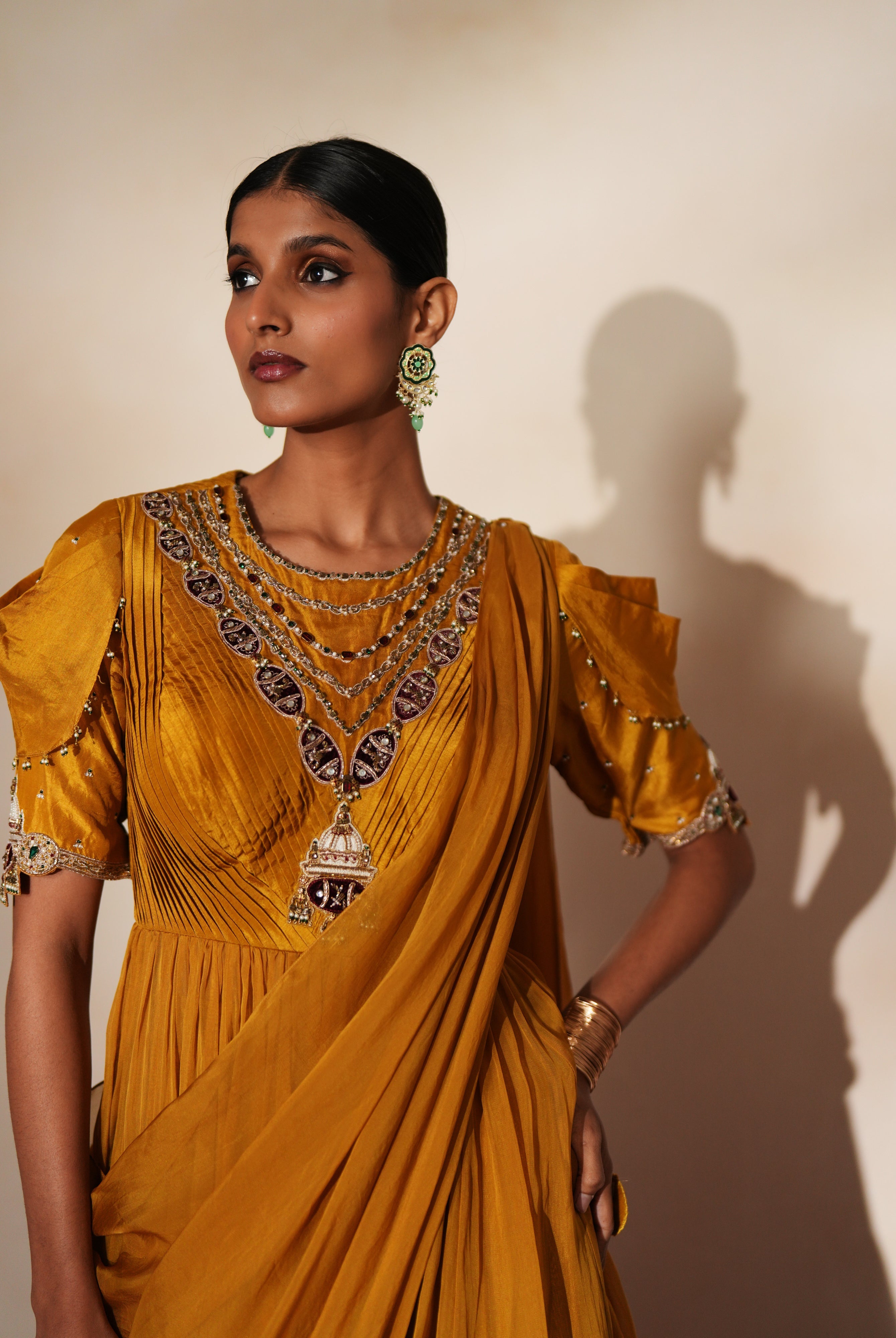 Woman in a golden yellow traditional outfit standing againsta beige wall on a red carpet.