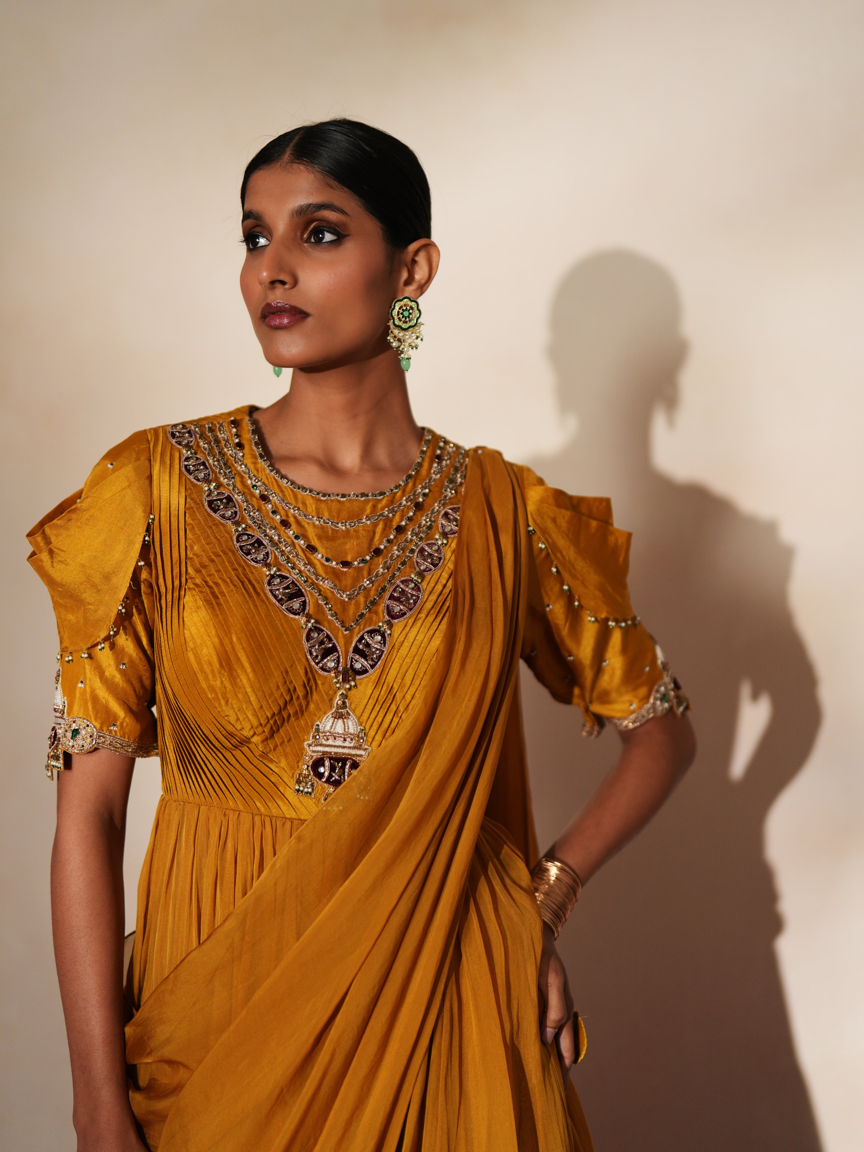 Woman in a golden yellow traditional outfit standing againsta beige wall on a red carpet.