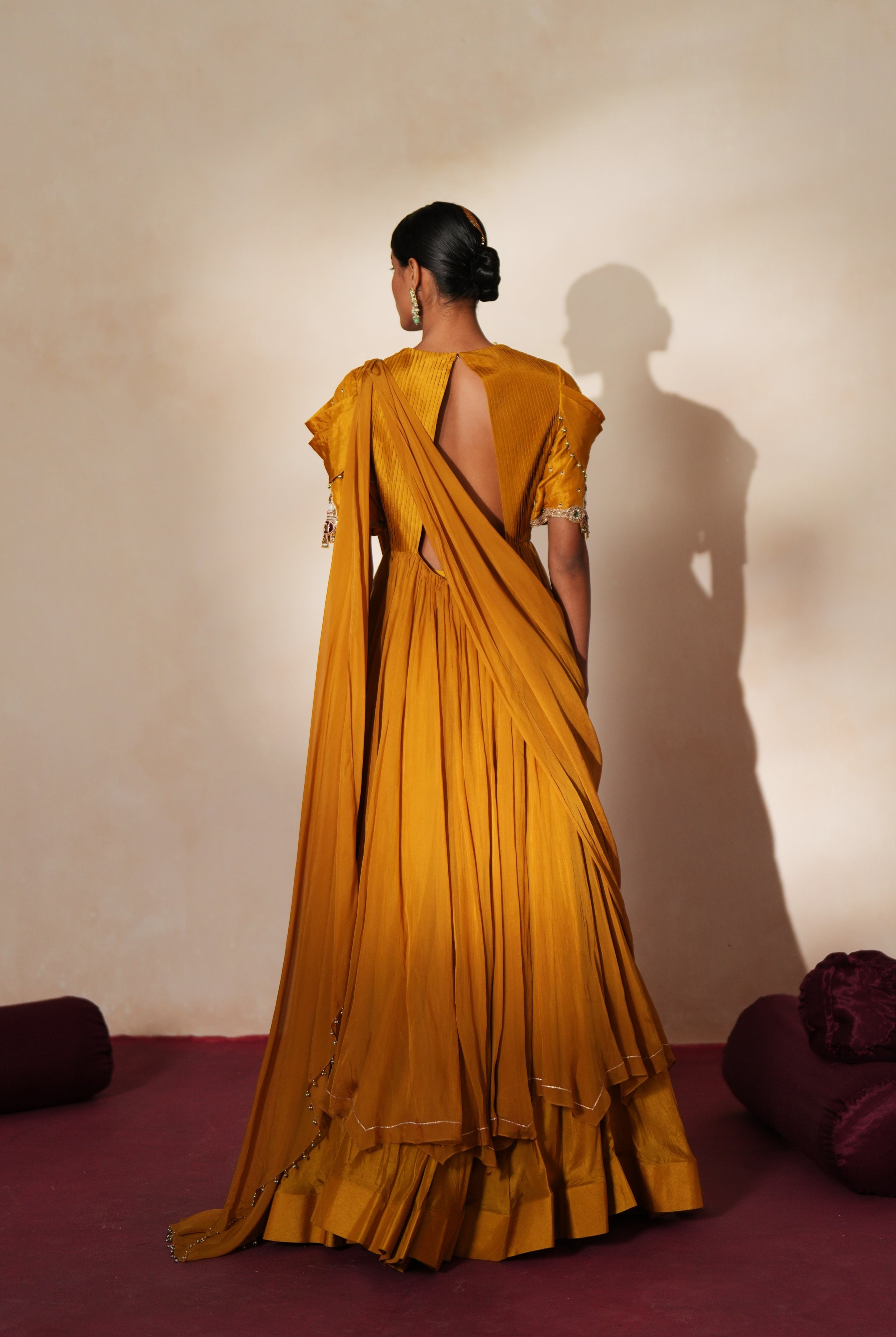 Woman in a golden yellow traditional outfit standing againsta beige wall on a red carpet.