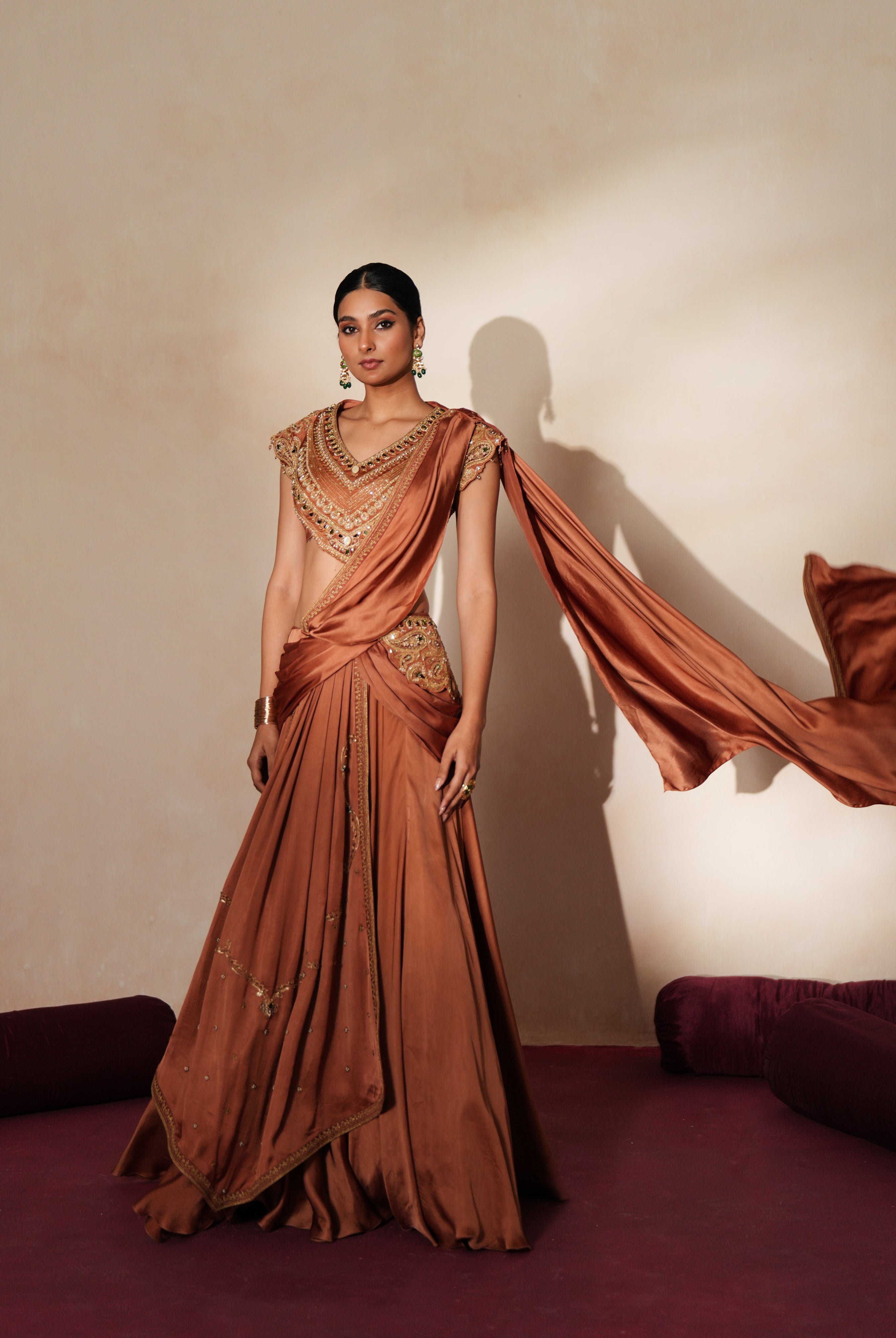 Woman in a metallic mocha traditional outfit standing againsta beige wall on a red carpet.