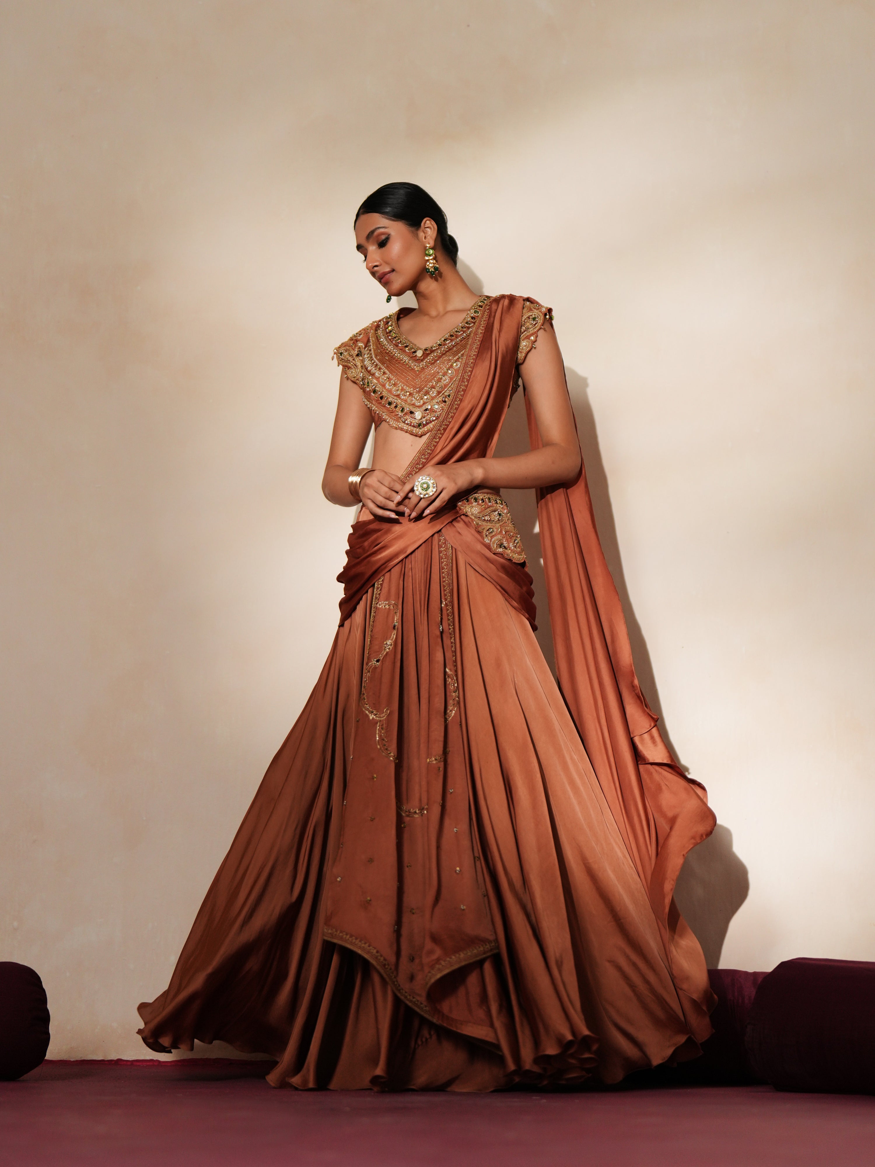 Woman in a metallic mocha traditional outfit standing againsta beige wall on a red carpet.