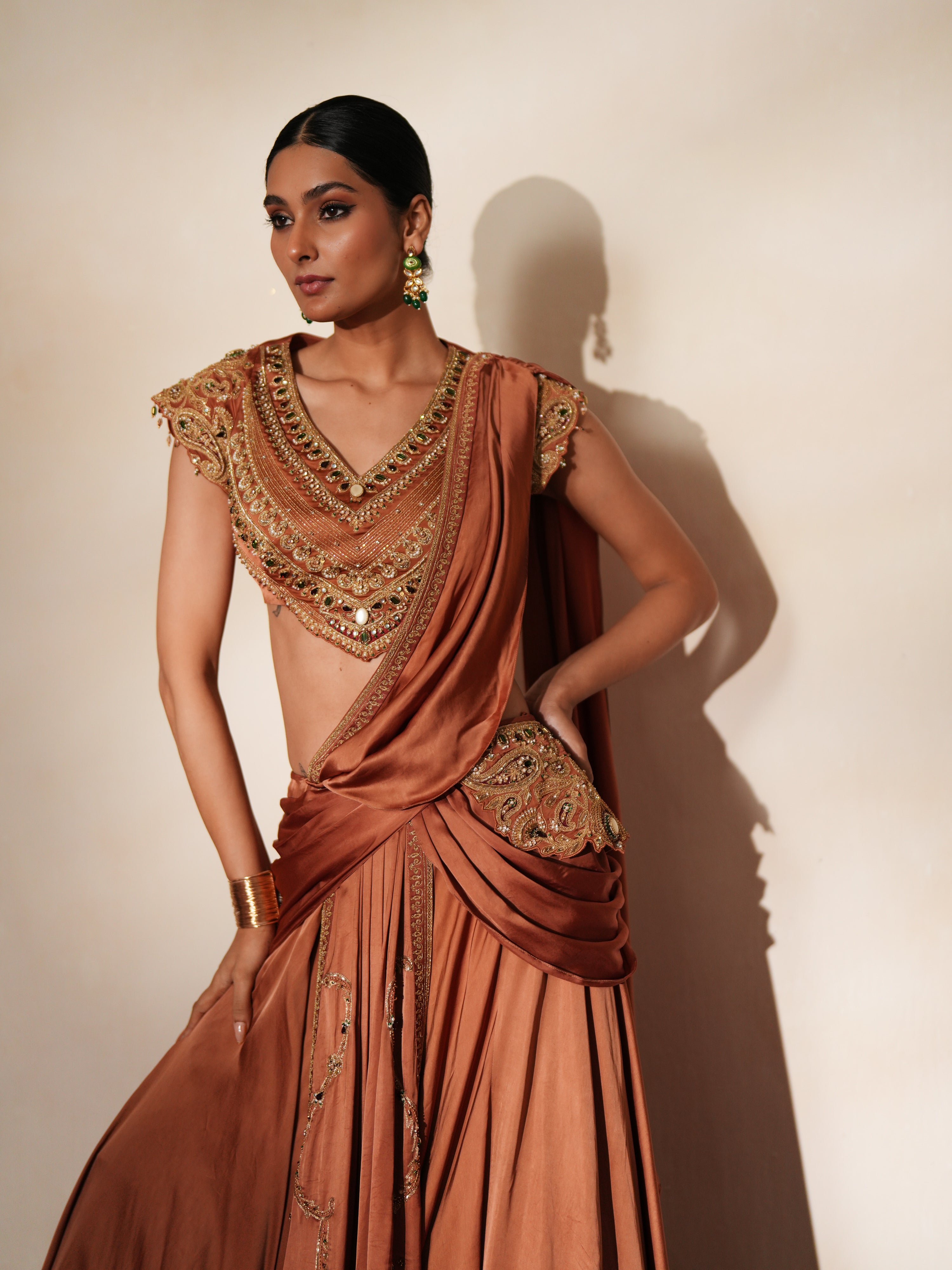 Woman in a metallic mocha traditional outfit standing againsta beige wall on a red carpet.