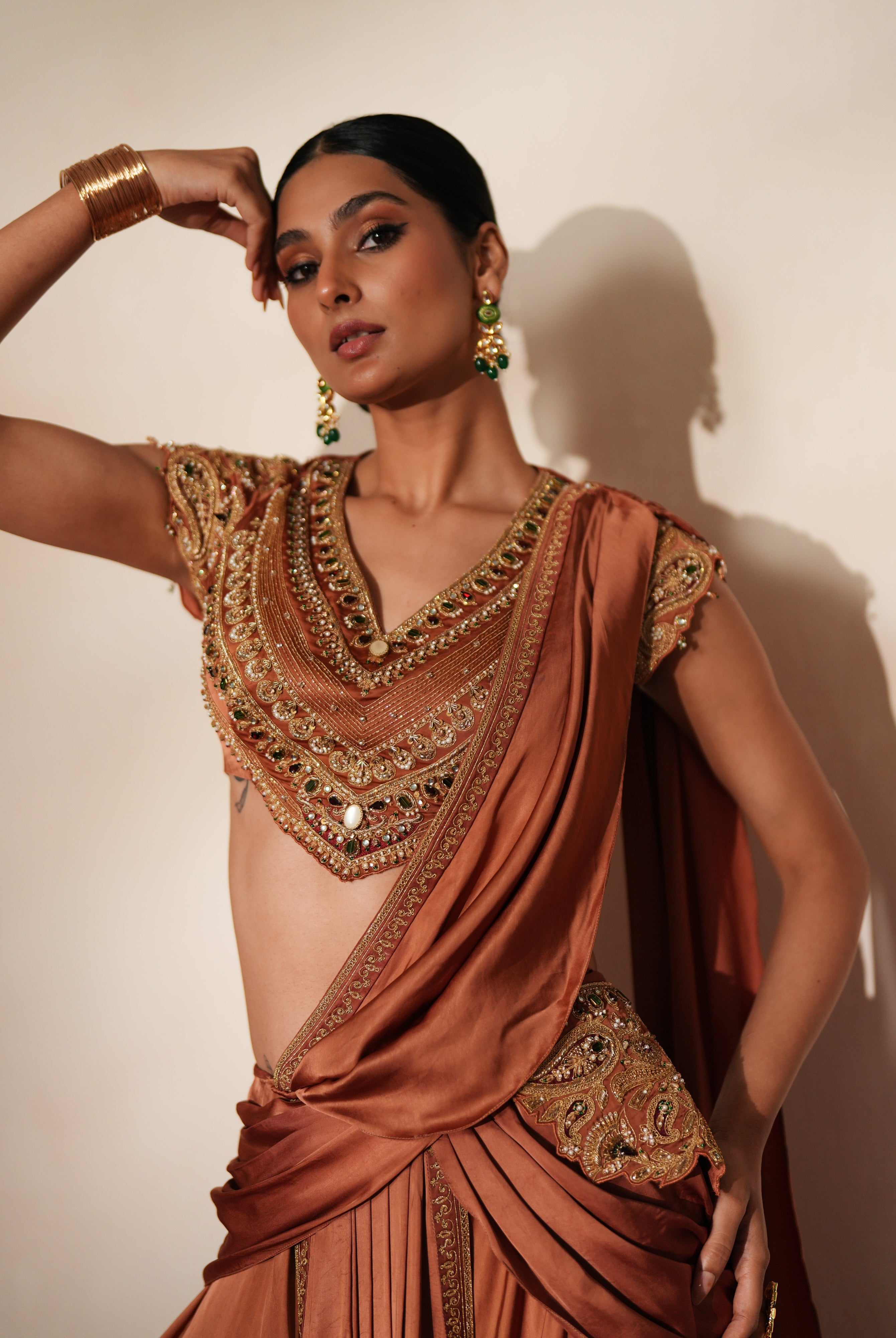 Woman in a metallic mocha traditional outfit standing againsta beige wall on a red carpet.