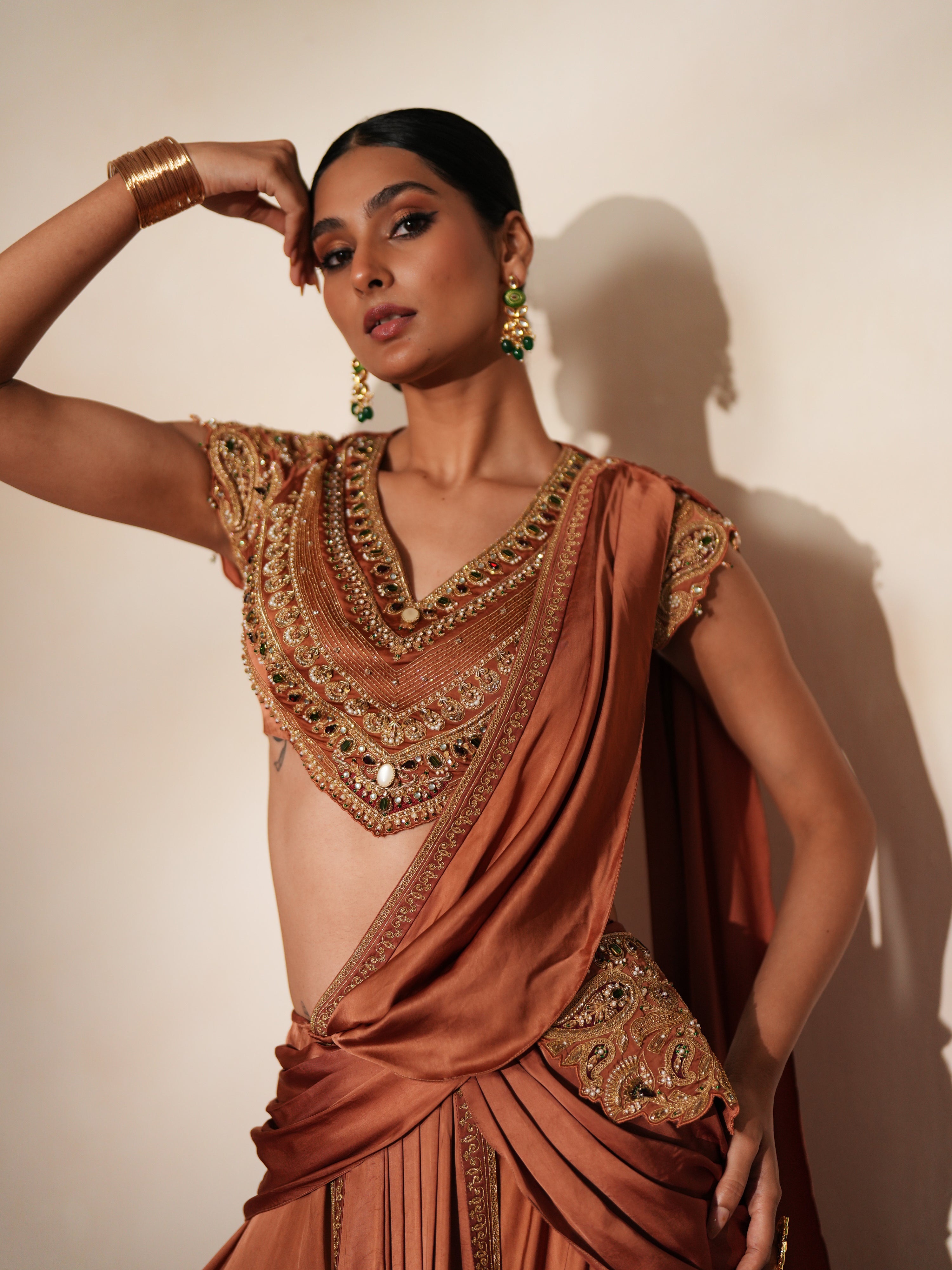 Woman in a metallic mocha traditional outfit standing againsta beige wall on a red carpet.