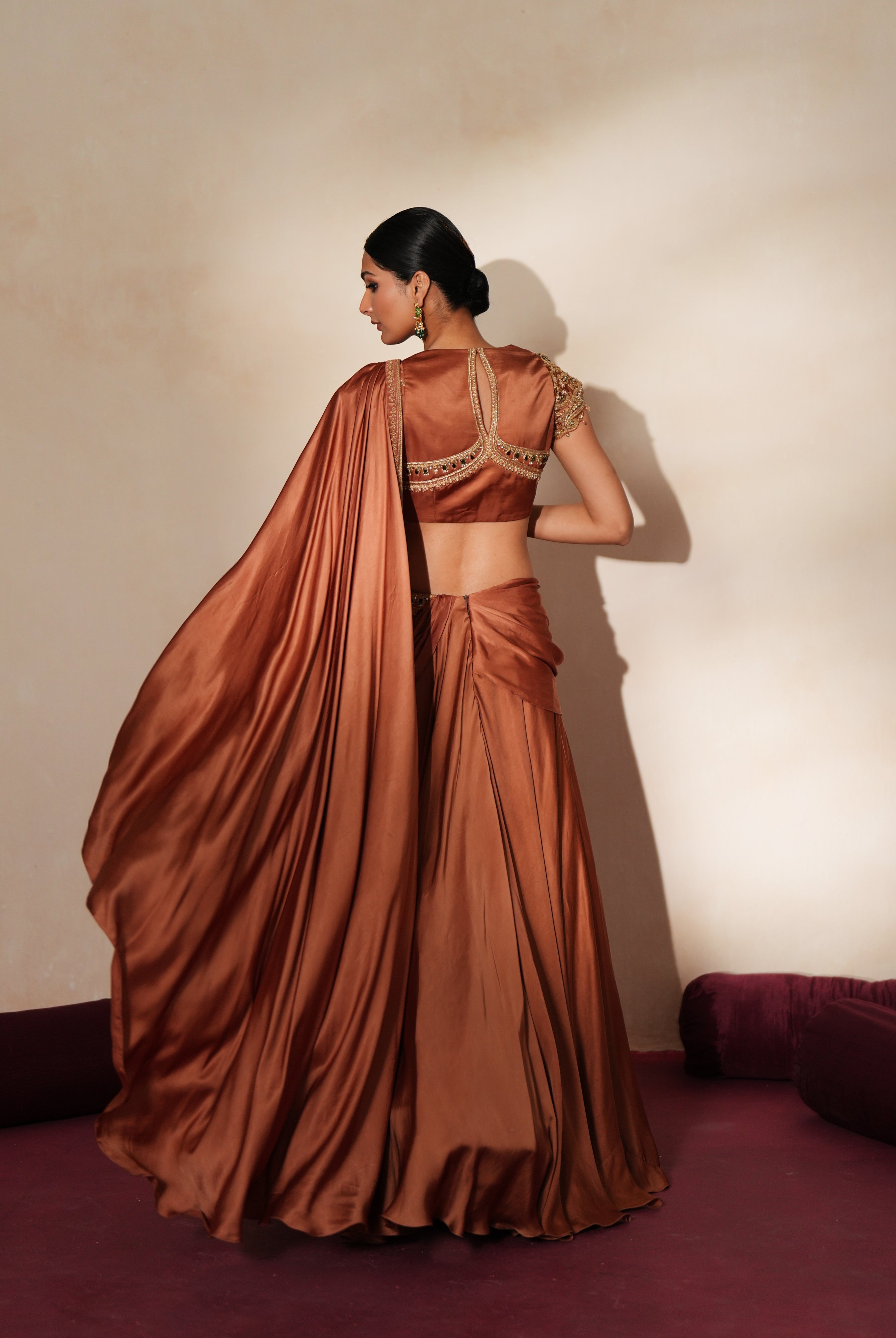 Woman in a metallic mocha traditional outfit standing againsta beige wall on a red carpet.