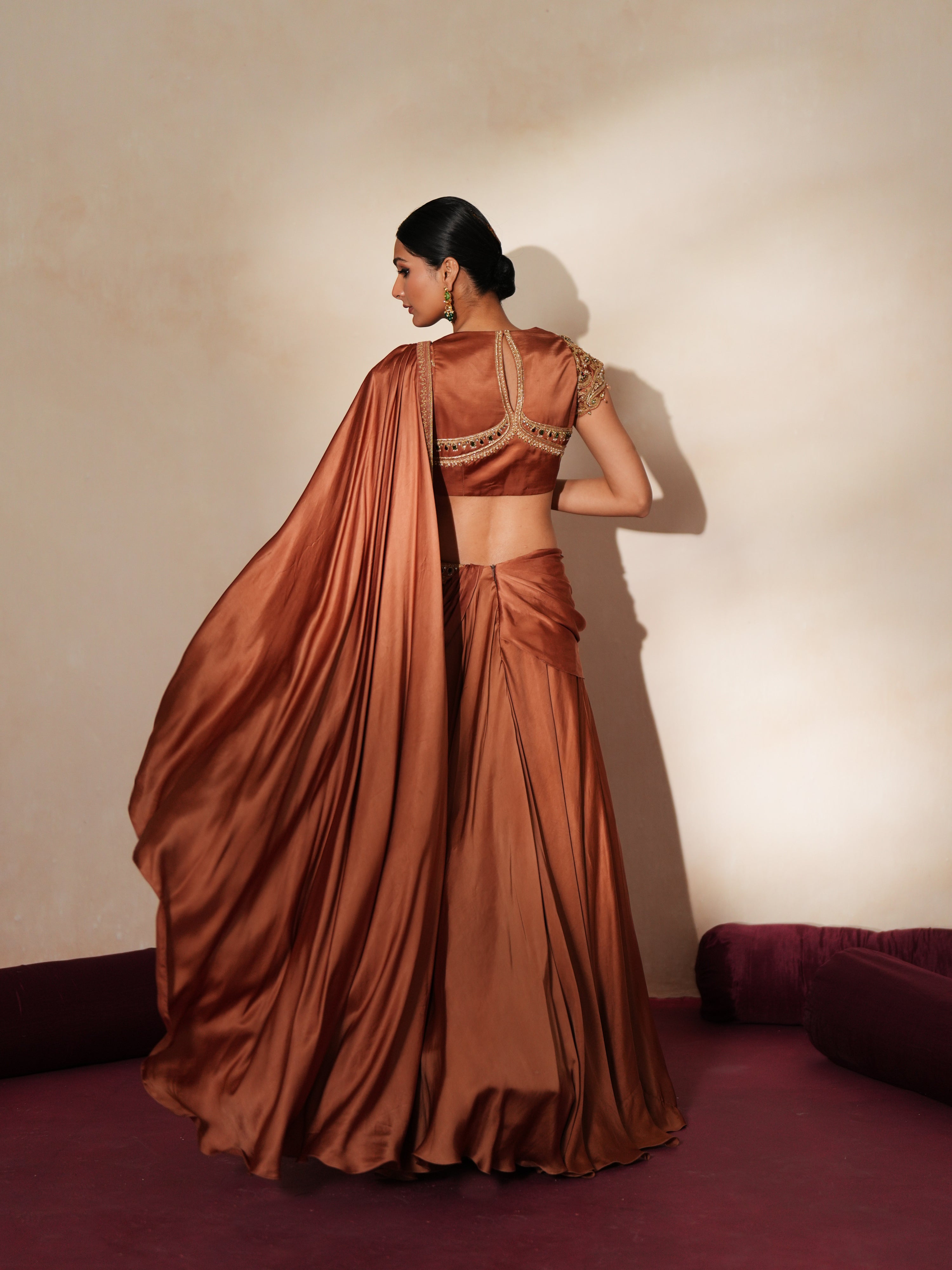 Woman in a metallic mocha traditional outfit standing againsta beige wall on a red carpet.