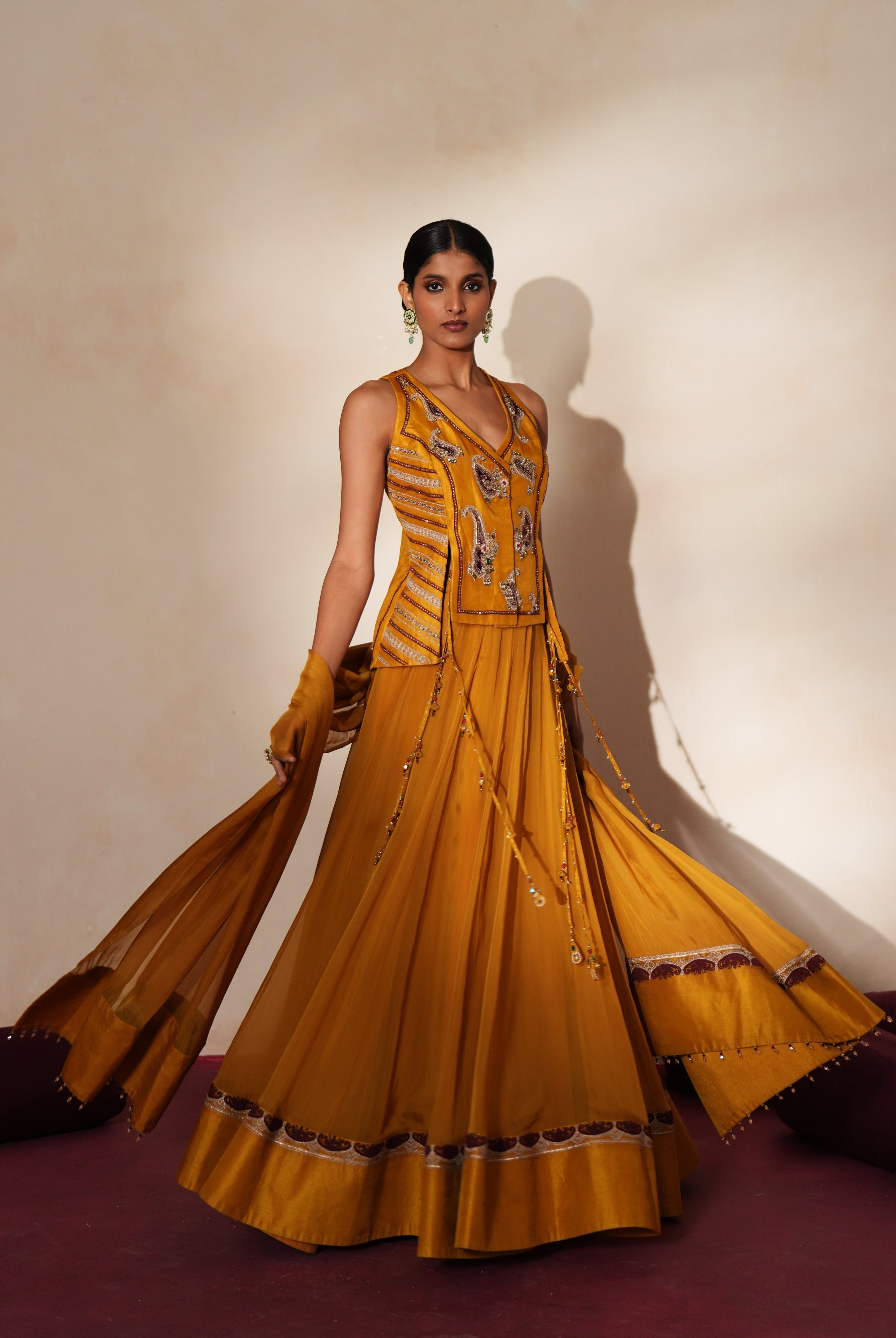Woman in a golden yellow traditional outfit standing againsta beige wall on a red carpet.