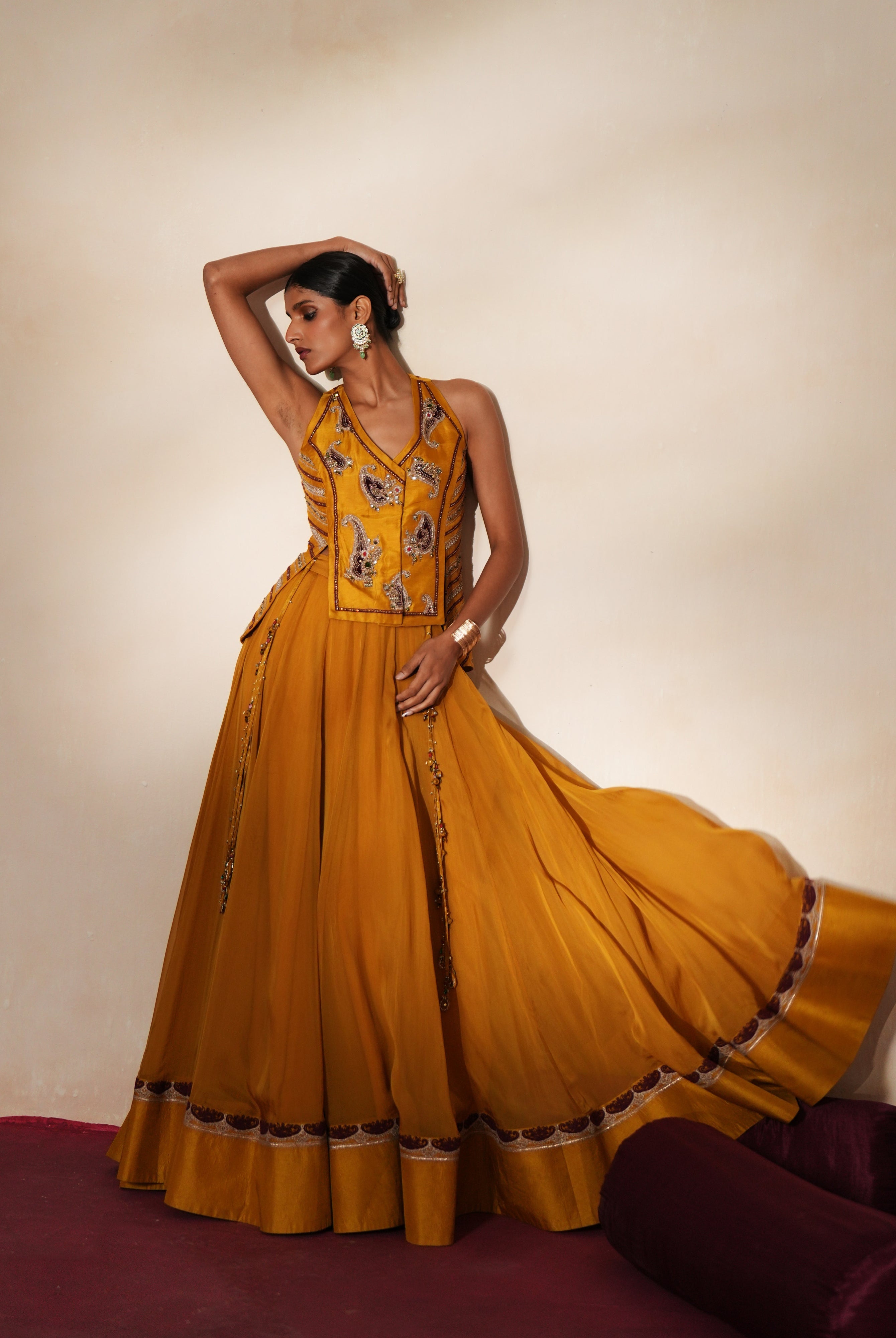 Woman in a golden yellow traditional outfit standing againsta beige wall on a red carpet.
