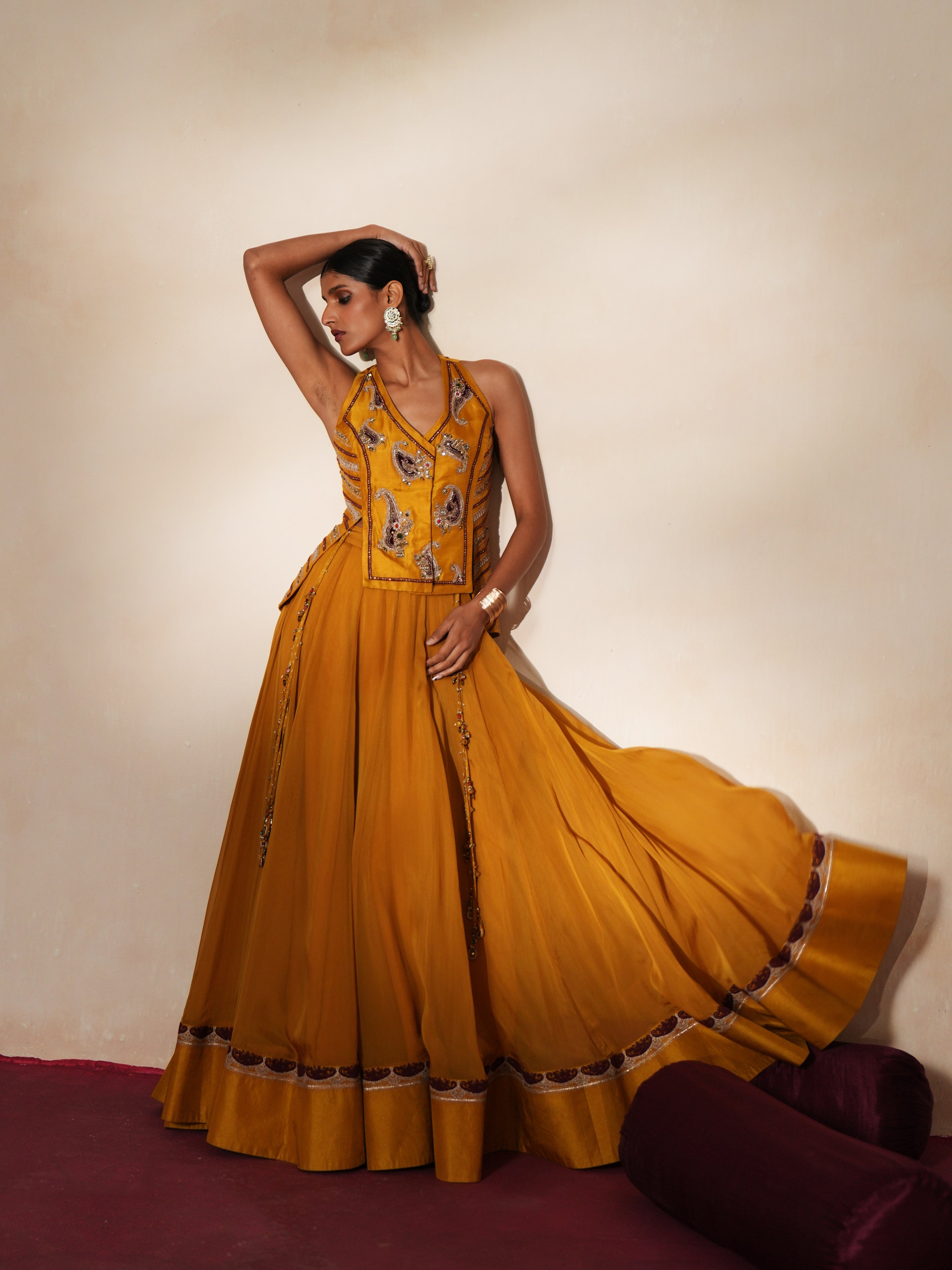 Woman in a golden yellow traditional outfit standing againsta beige wall on a red carpet.