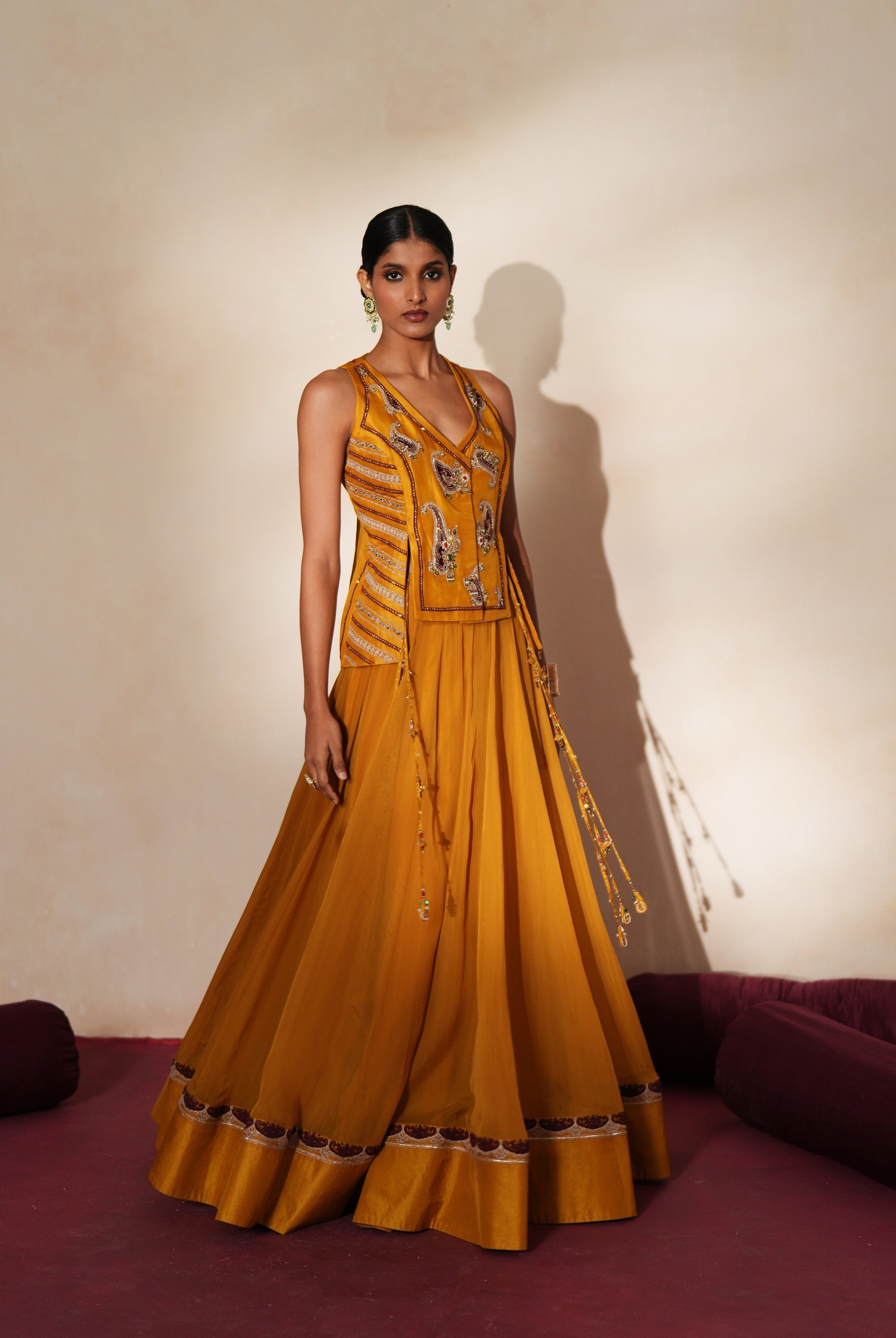 Woman in a golden yellow traditional outfit standing againsta beige wall on a red carpet.