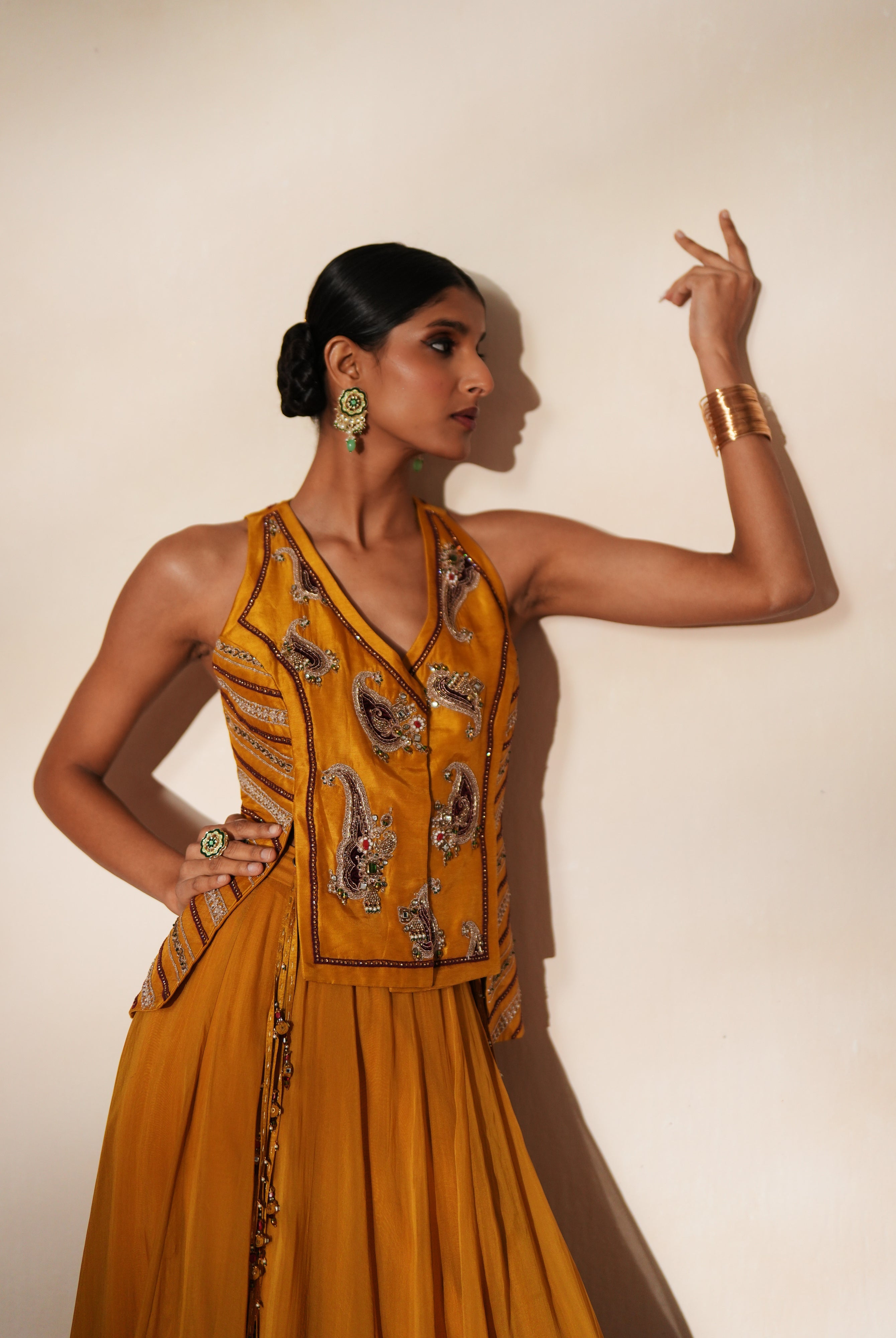 Woman in a golden yellow traditional outfit standing againsta beige wall on a red carpet.