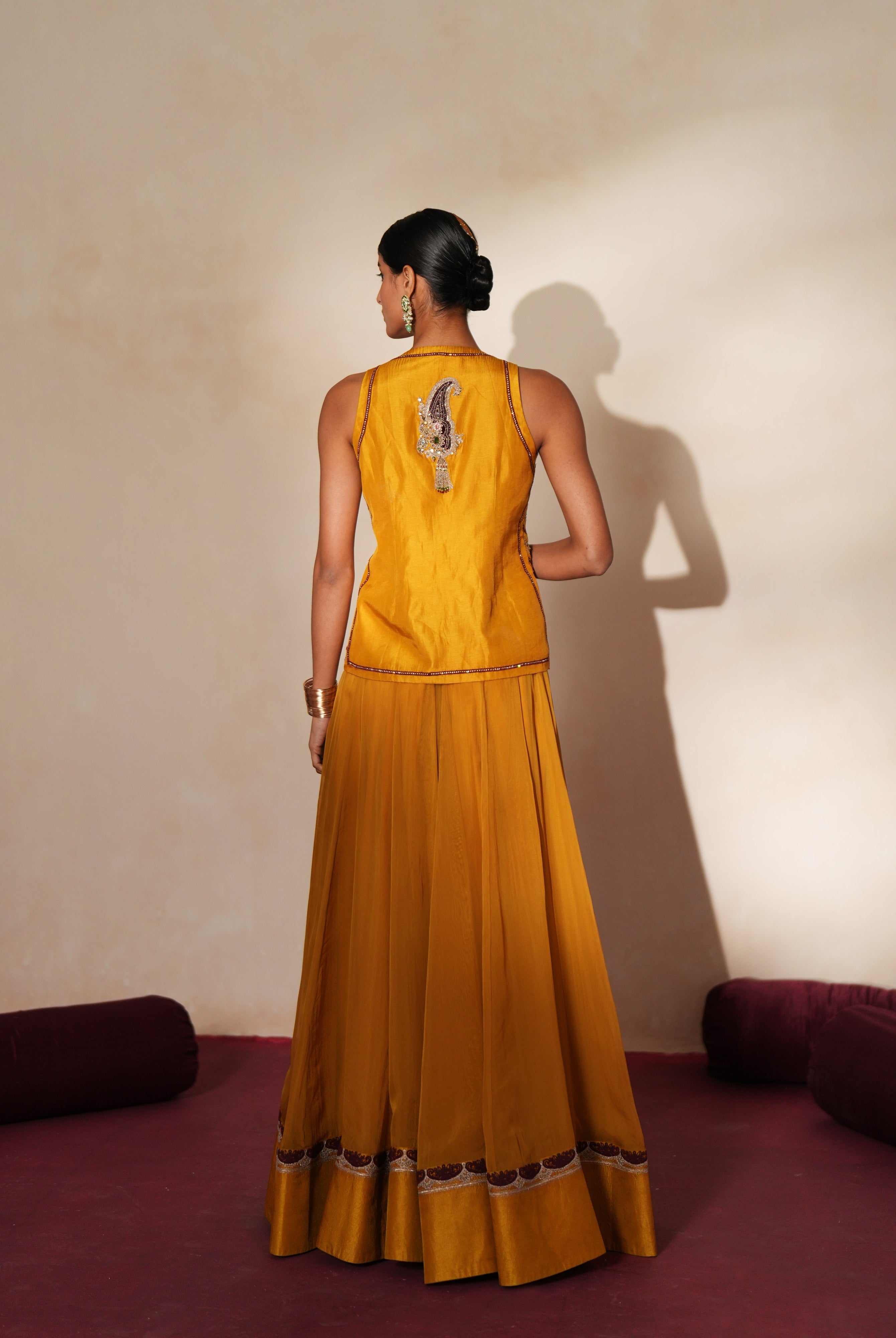 Woman in a golden yellow traditional outfit standing againsta beige wall on a red carpet.