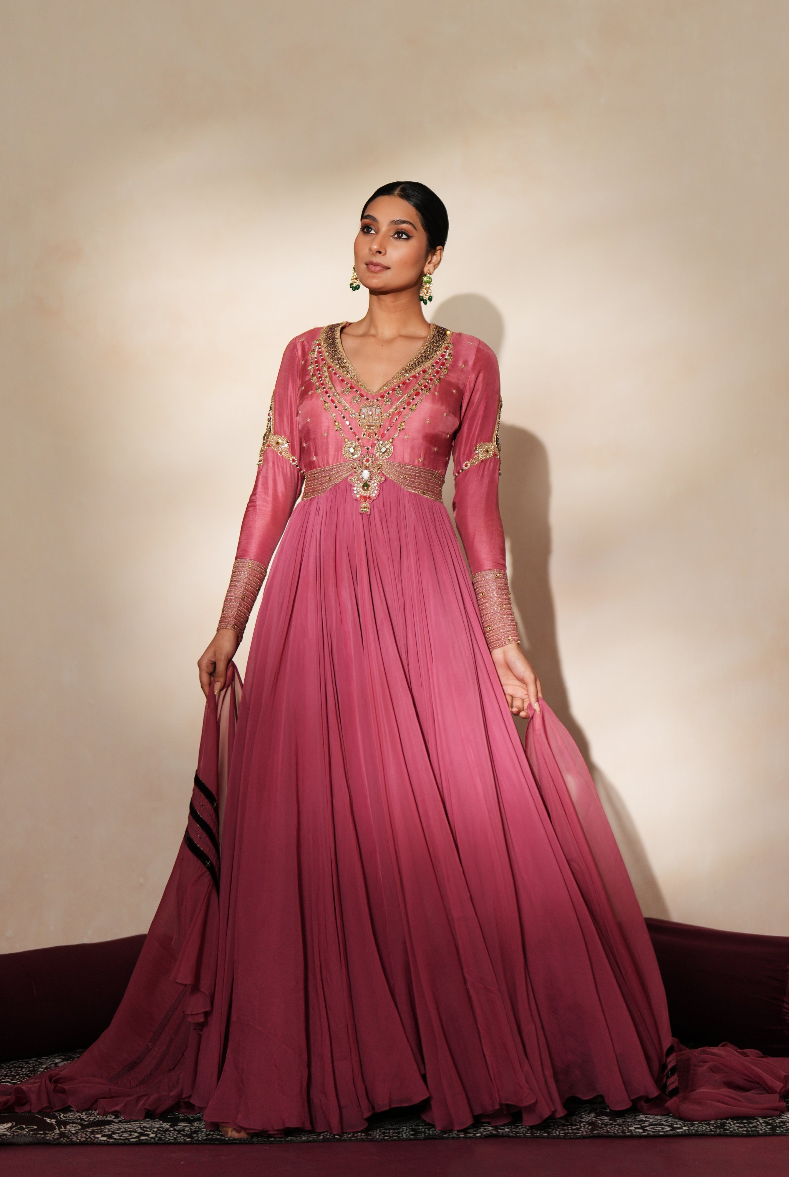 Woman in a mauve pink traditional outfit standing againsta beige wall on a red carpet.