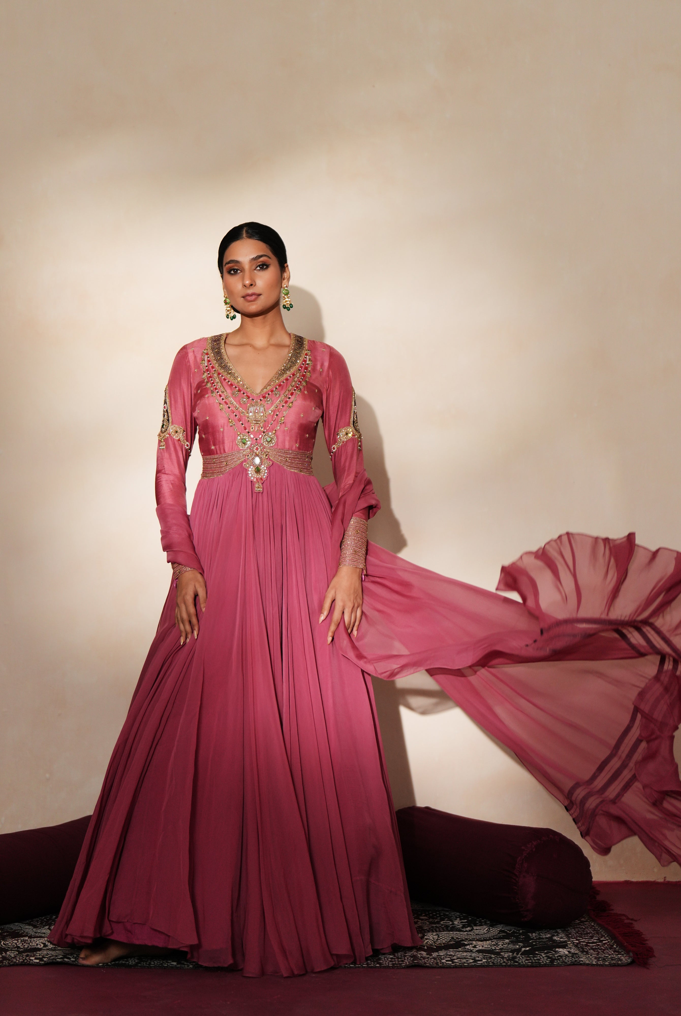 Woman in a mauve pink traditional outfit standing againsta beige wall on a red carpet.