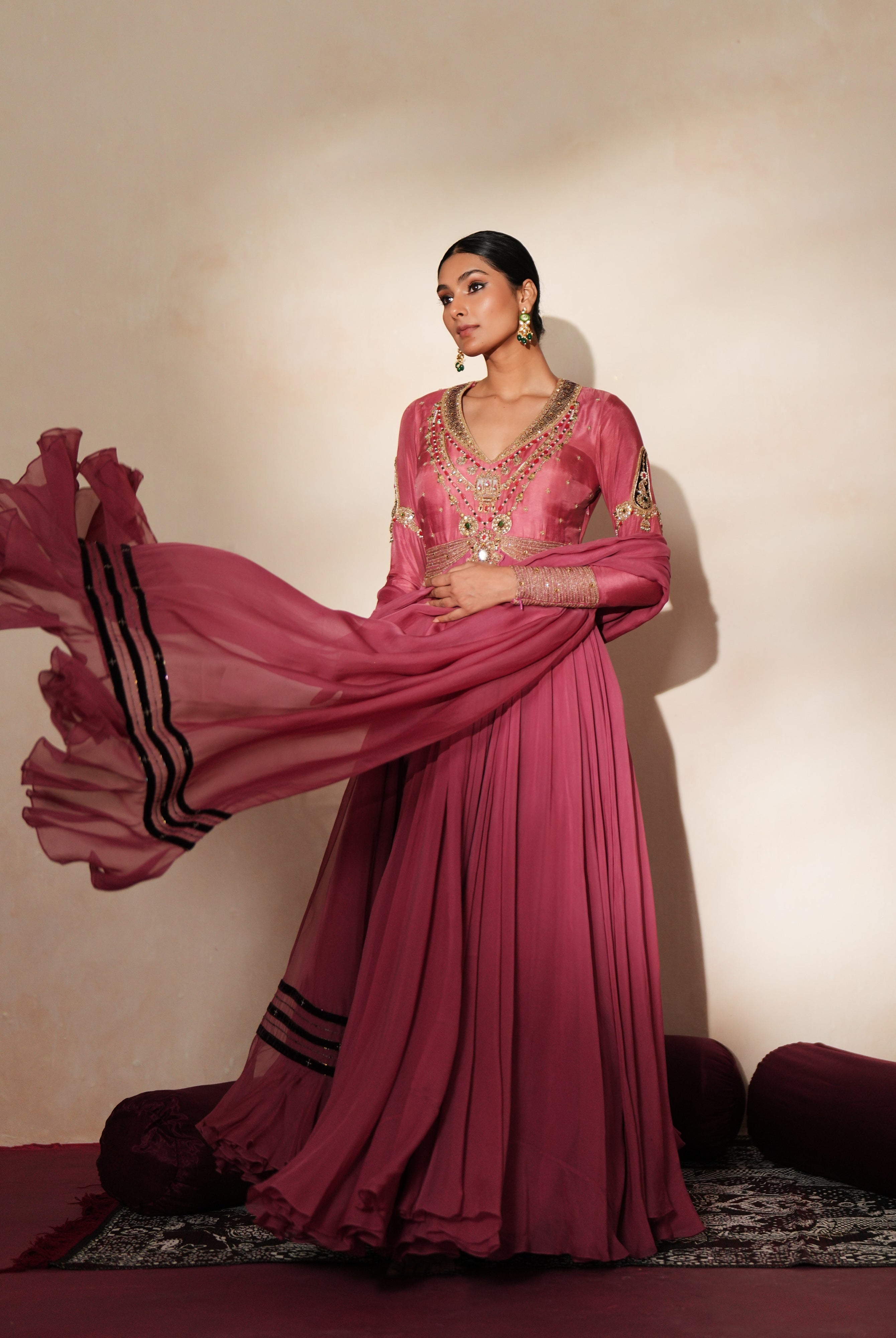 Woman in a mauve pink traditional outfit standing againsta beige wall on a red carpet.
