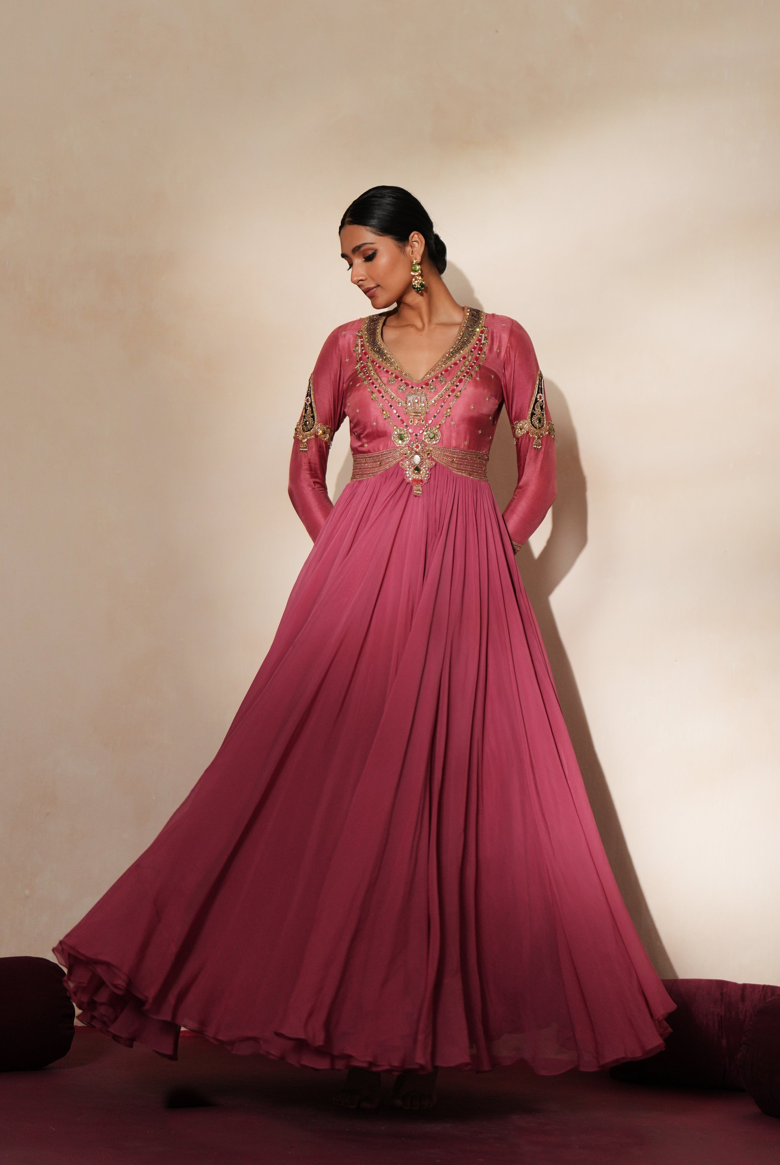 Woman in a mauve pink traditional outfit standing againsta beige wall on a red carpet.